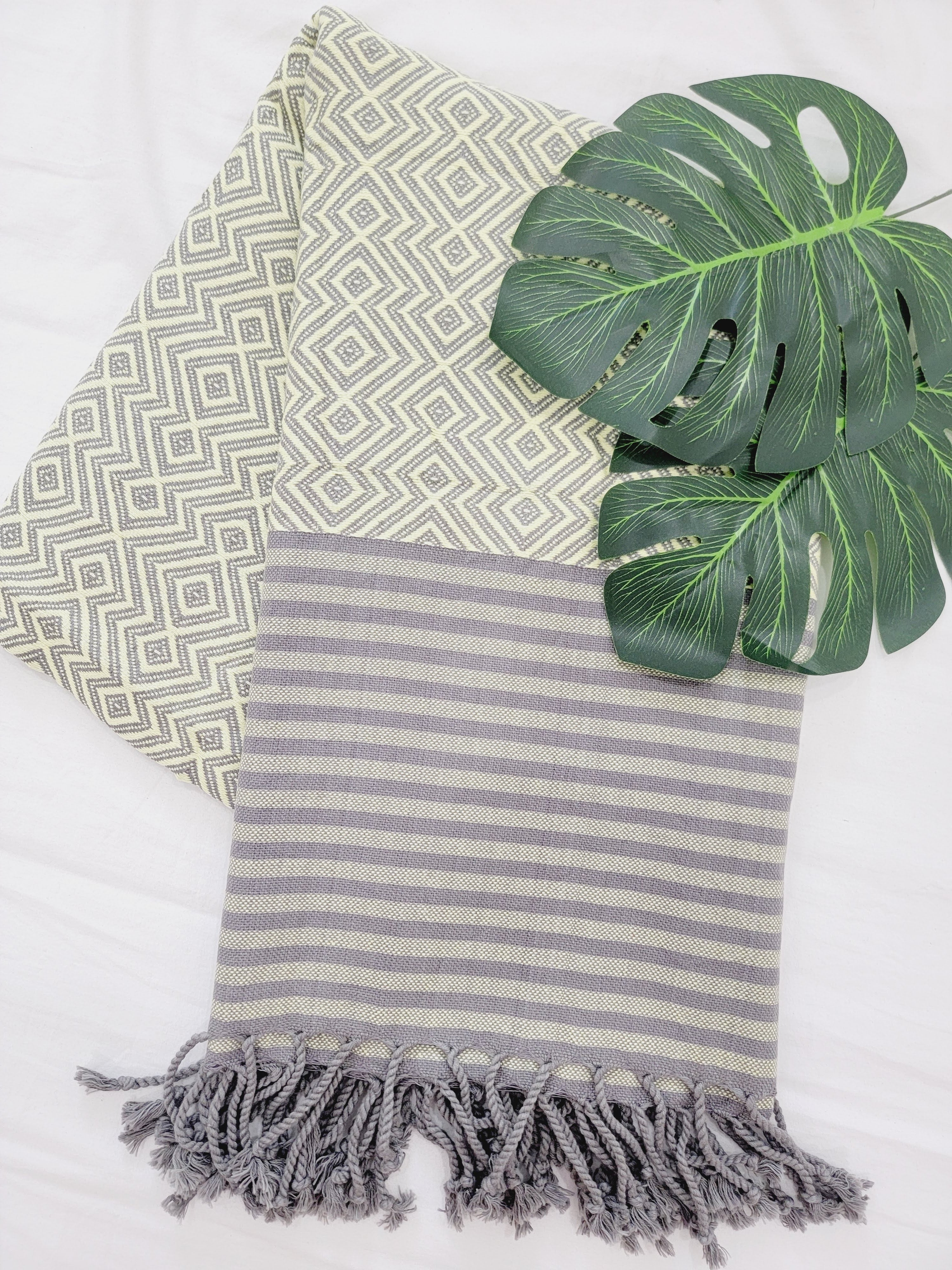 Two patterned towels with tassels and a green leaf on a white background