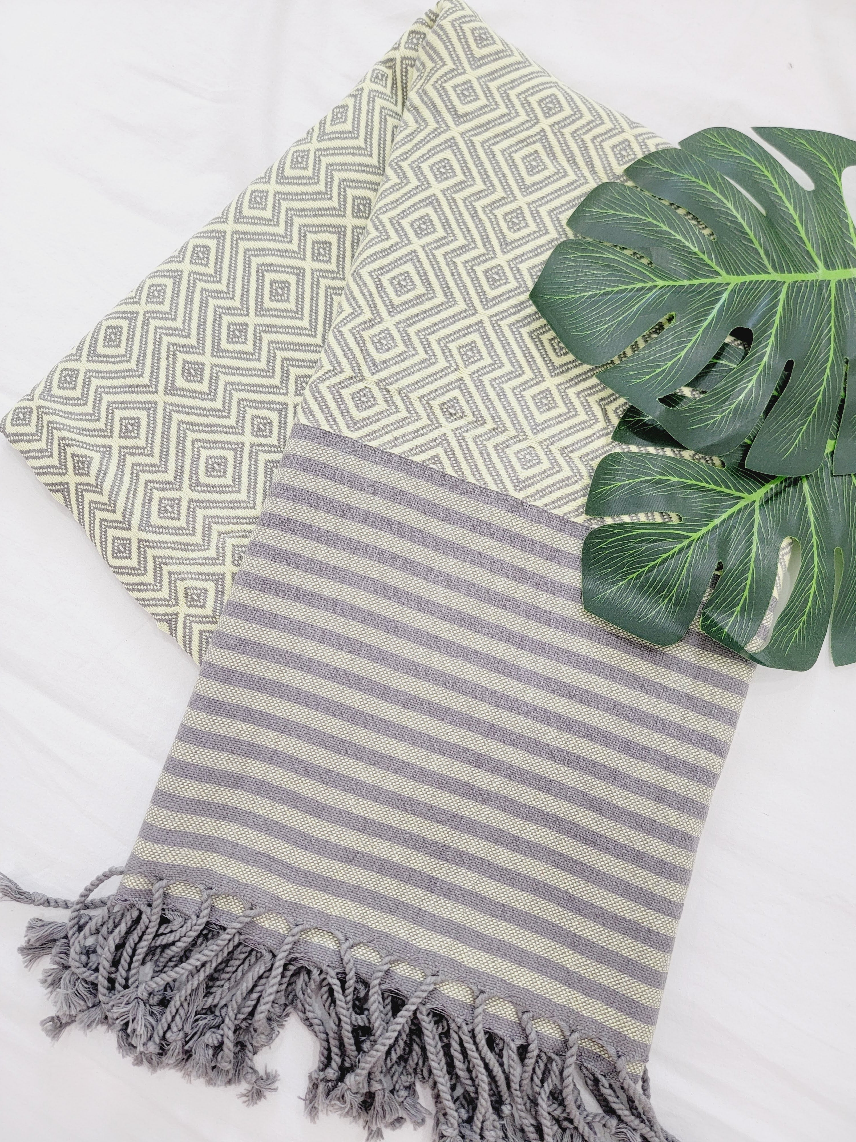 Two patterned towels with geometric and striped designs, accompanied by a green leaf on a white background.