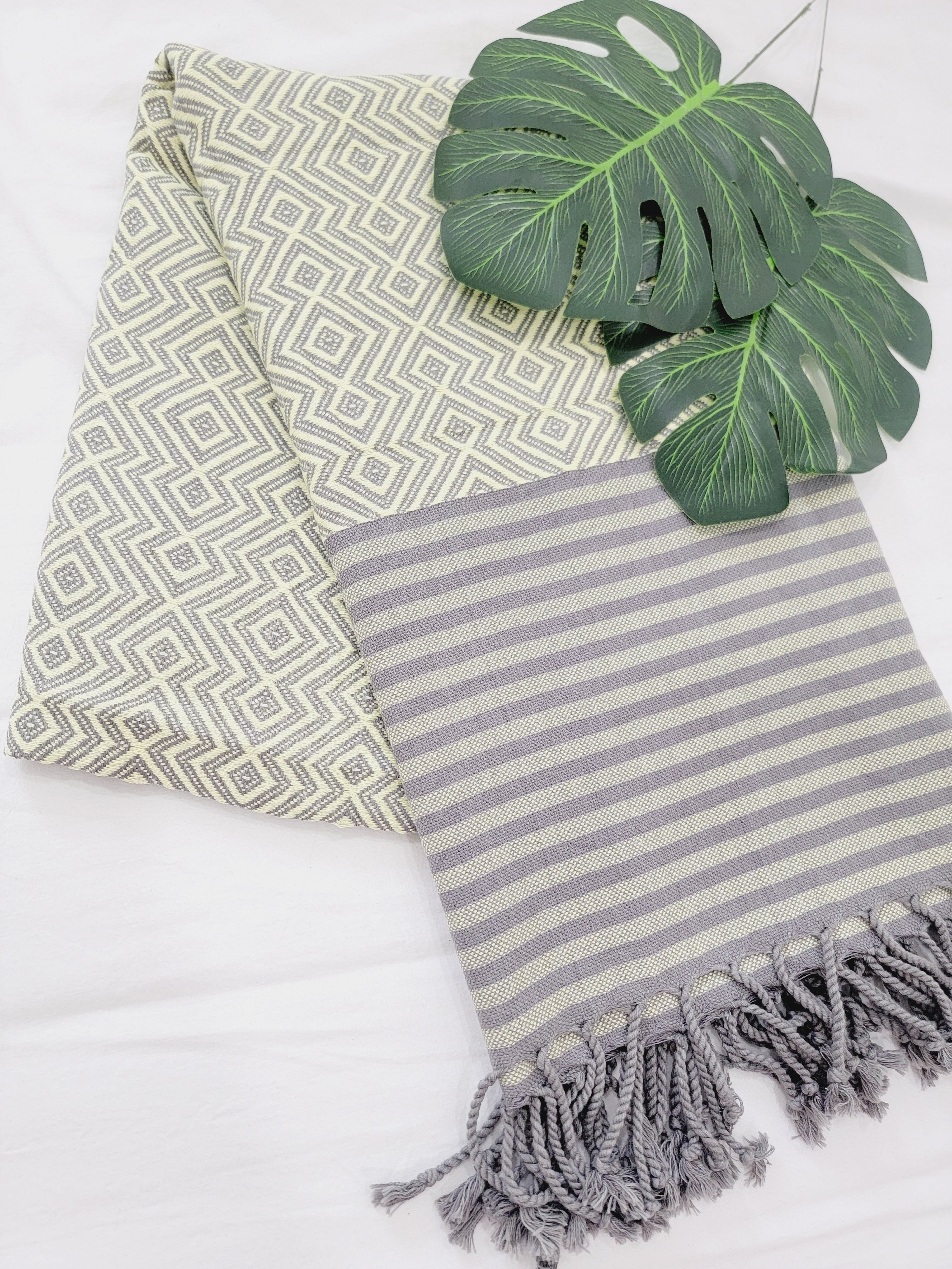 Two towels, one with a geometric pattern and the other with stripes and tassels, on a white background.