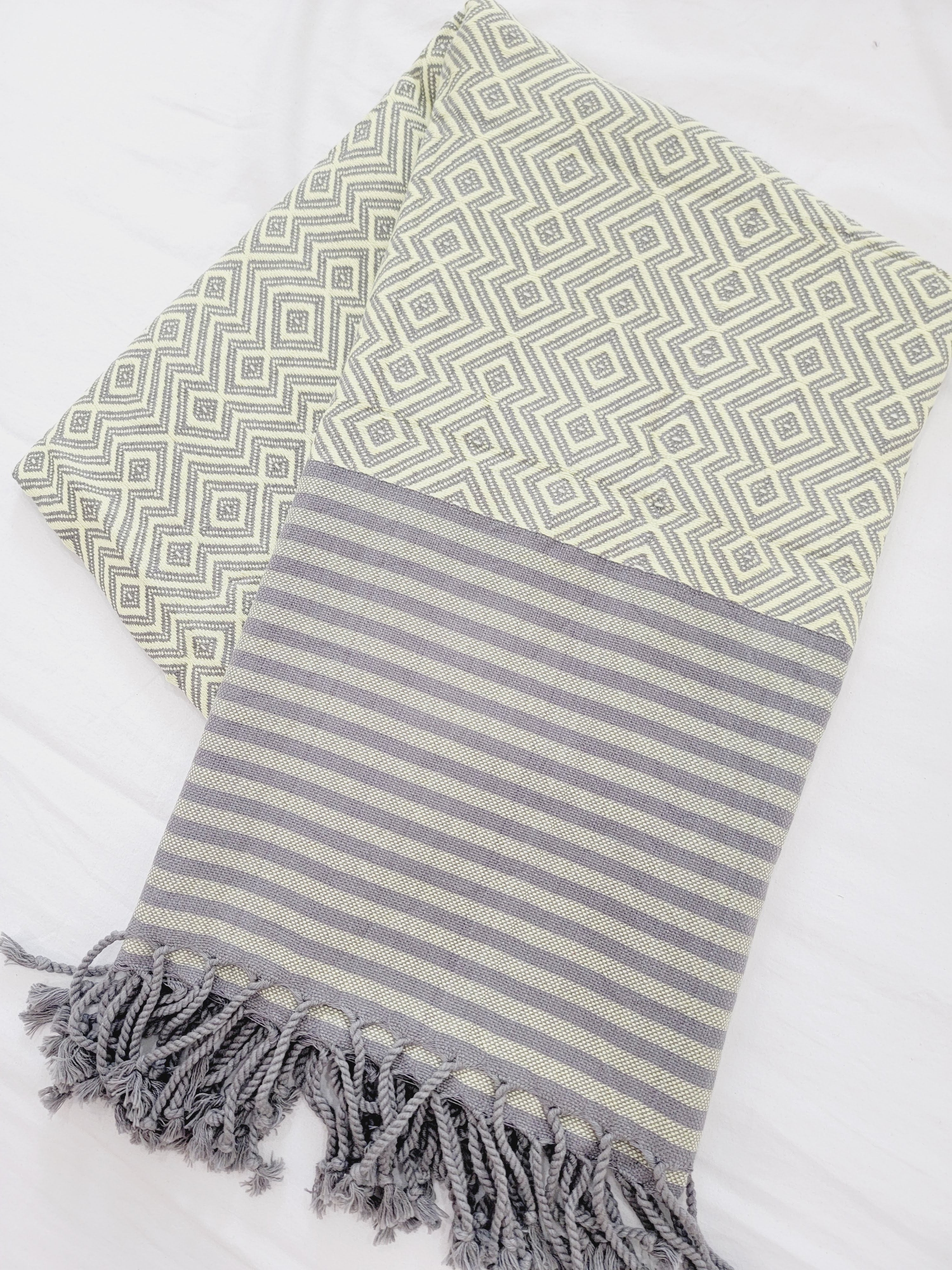 Two patterned towels, one green with geometric design and the other gray with stripes, on a white background.