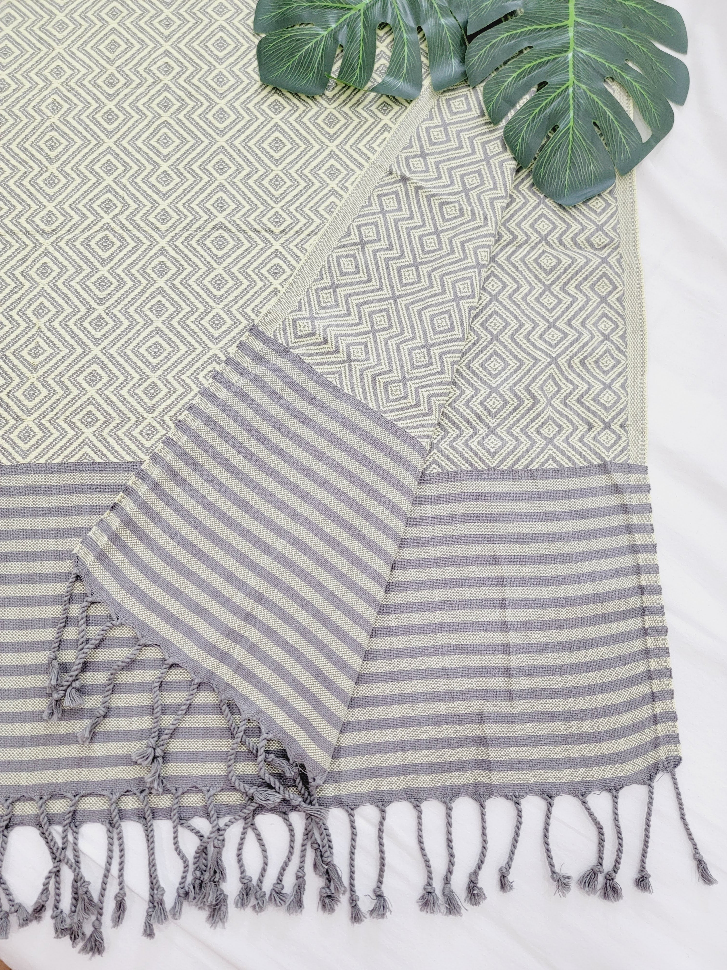 Striped towel with tassels on a textured surface with green leaves.