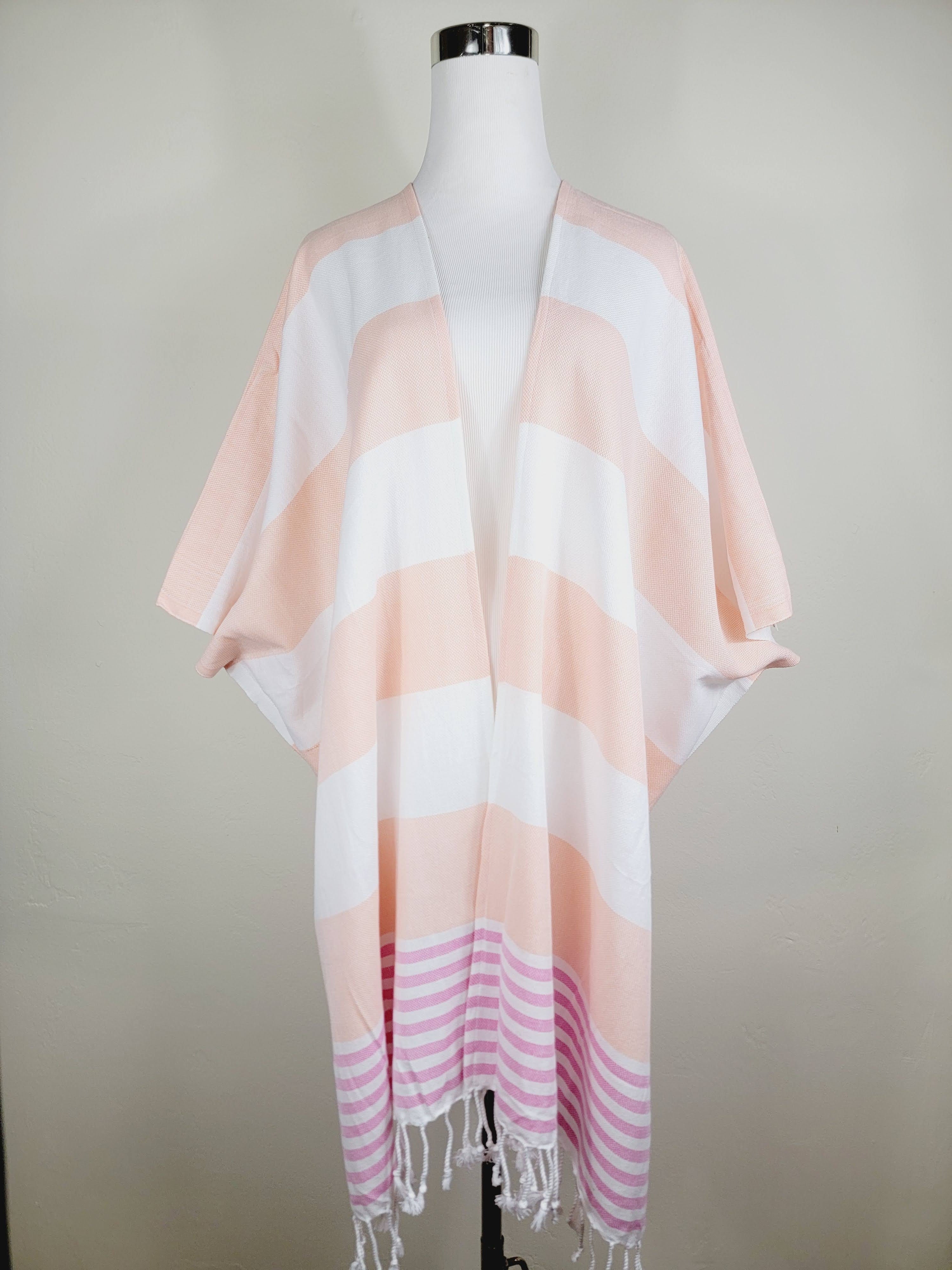 Mannequin wearing a light pink and white striped scarf with fringe on a plain background