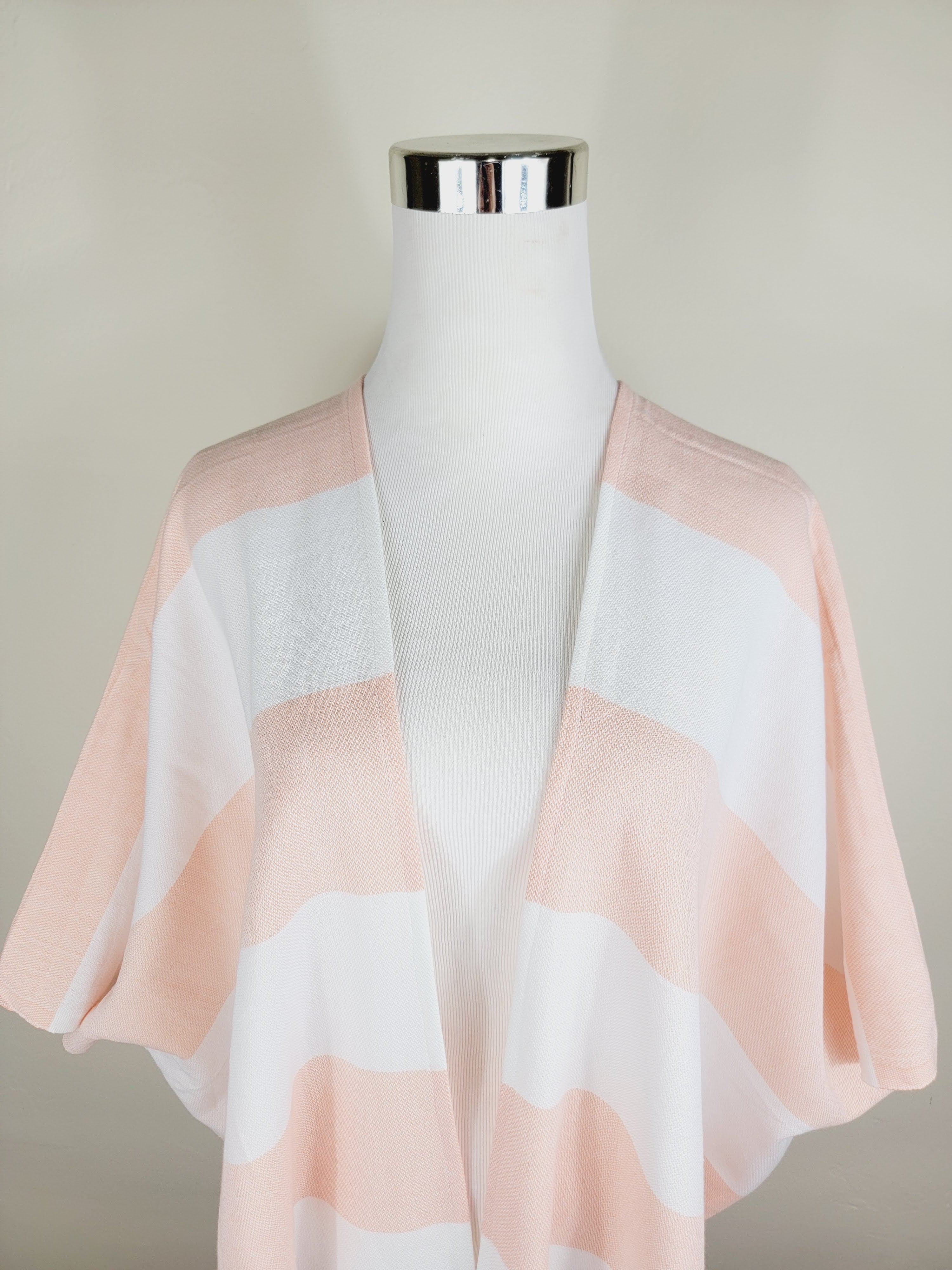 Mannequin wearing a light pink and white striped shawl against a plain background