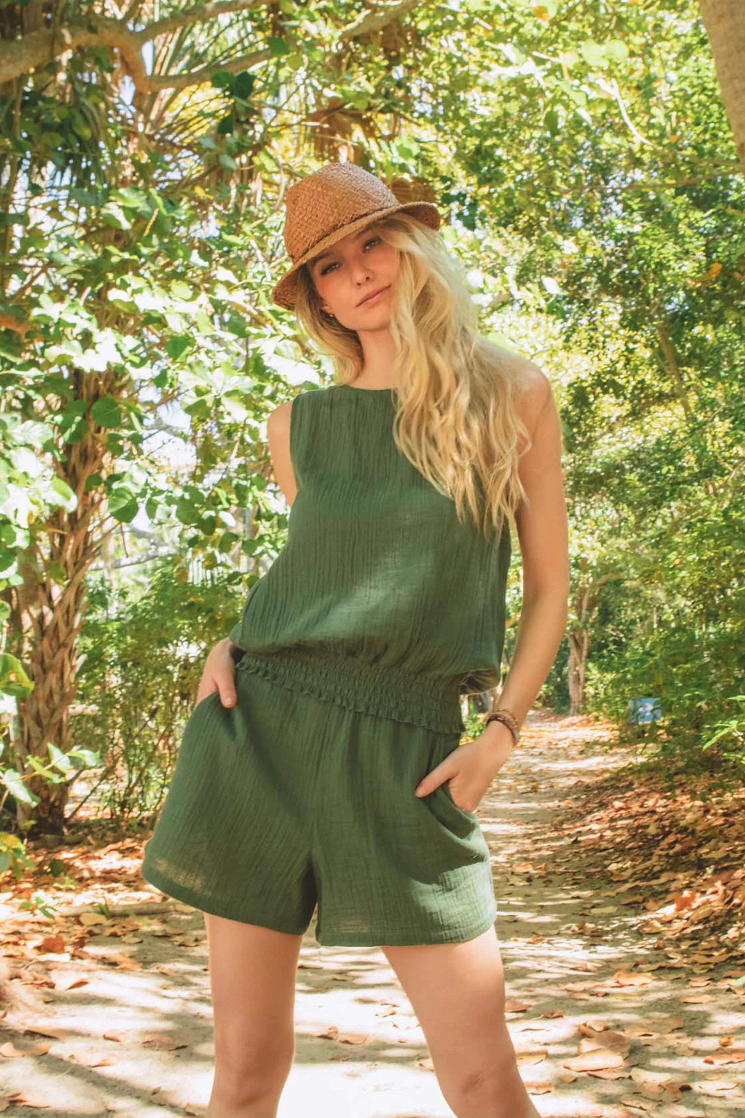Woman in a green romper and hat standing in a forest