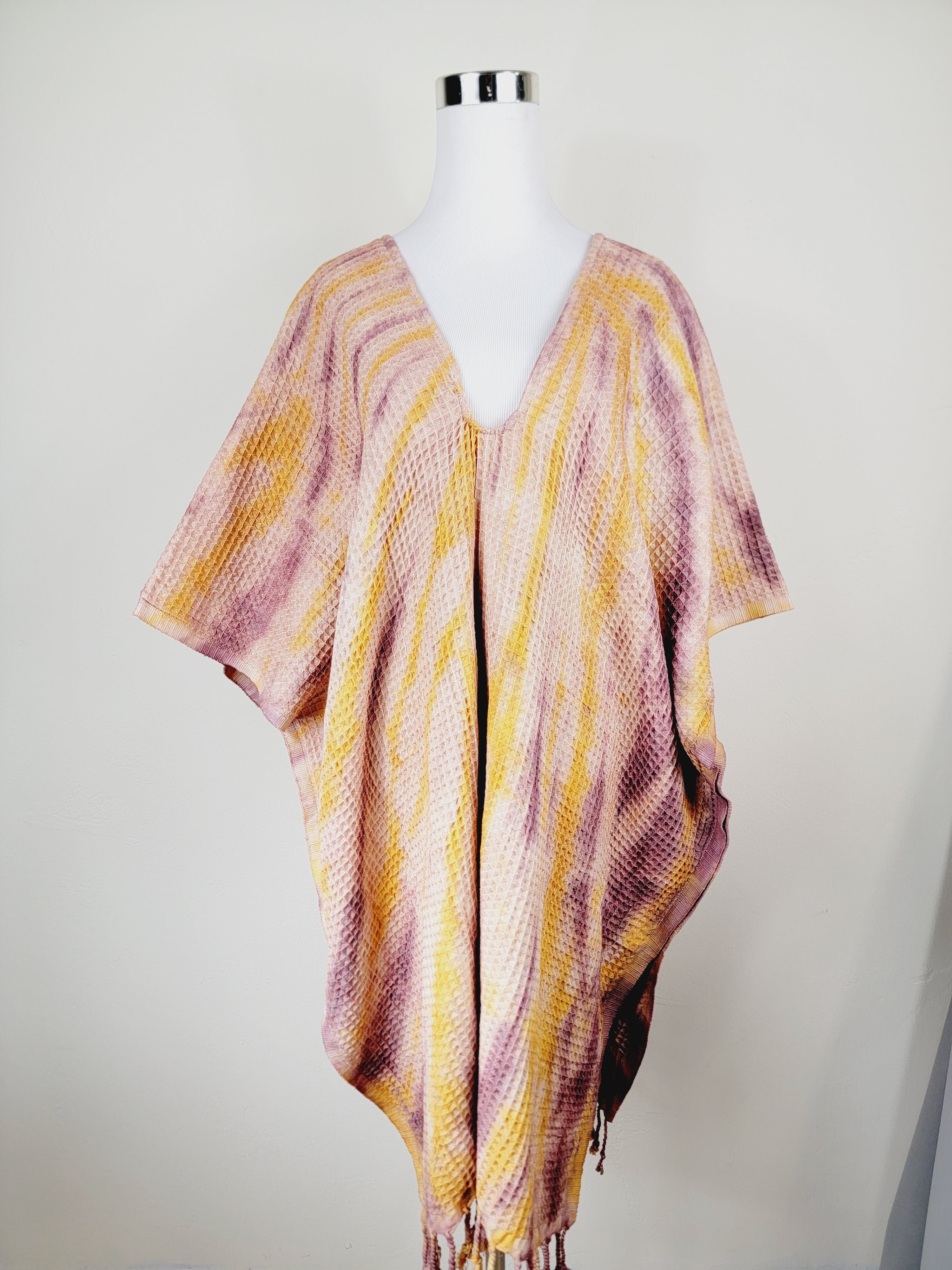 Mannequin wearing a colorful striped poncho against a plain background