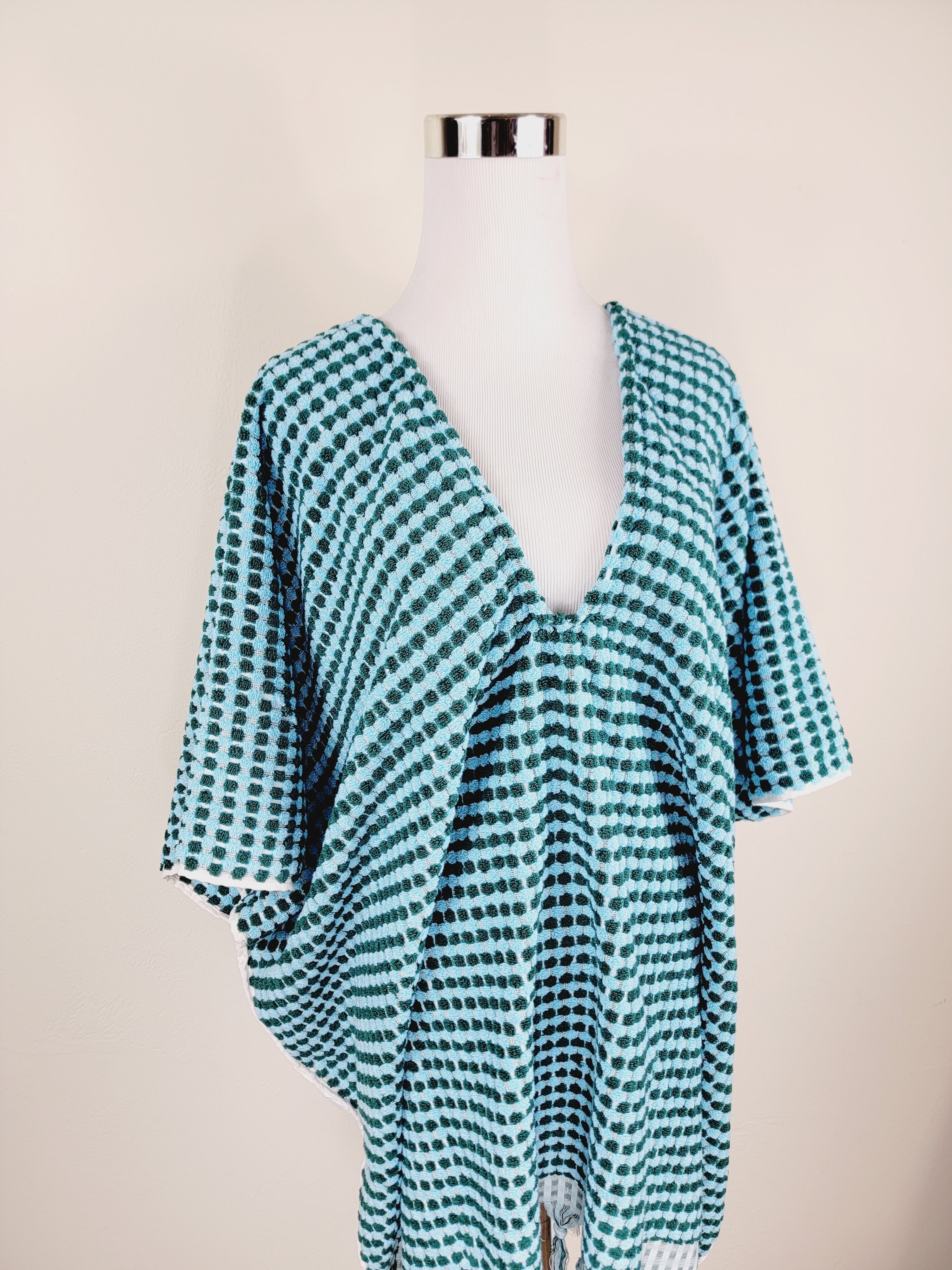 Green and white checkered poncho on a mannequin against a beige background
