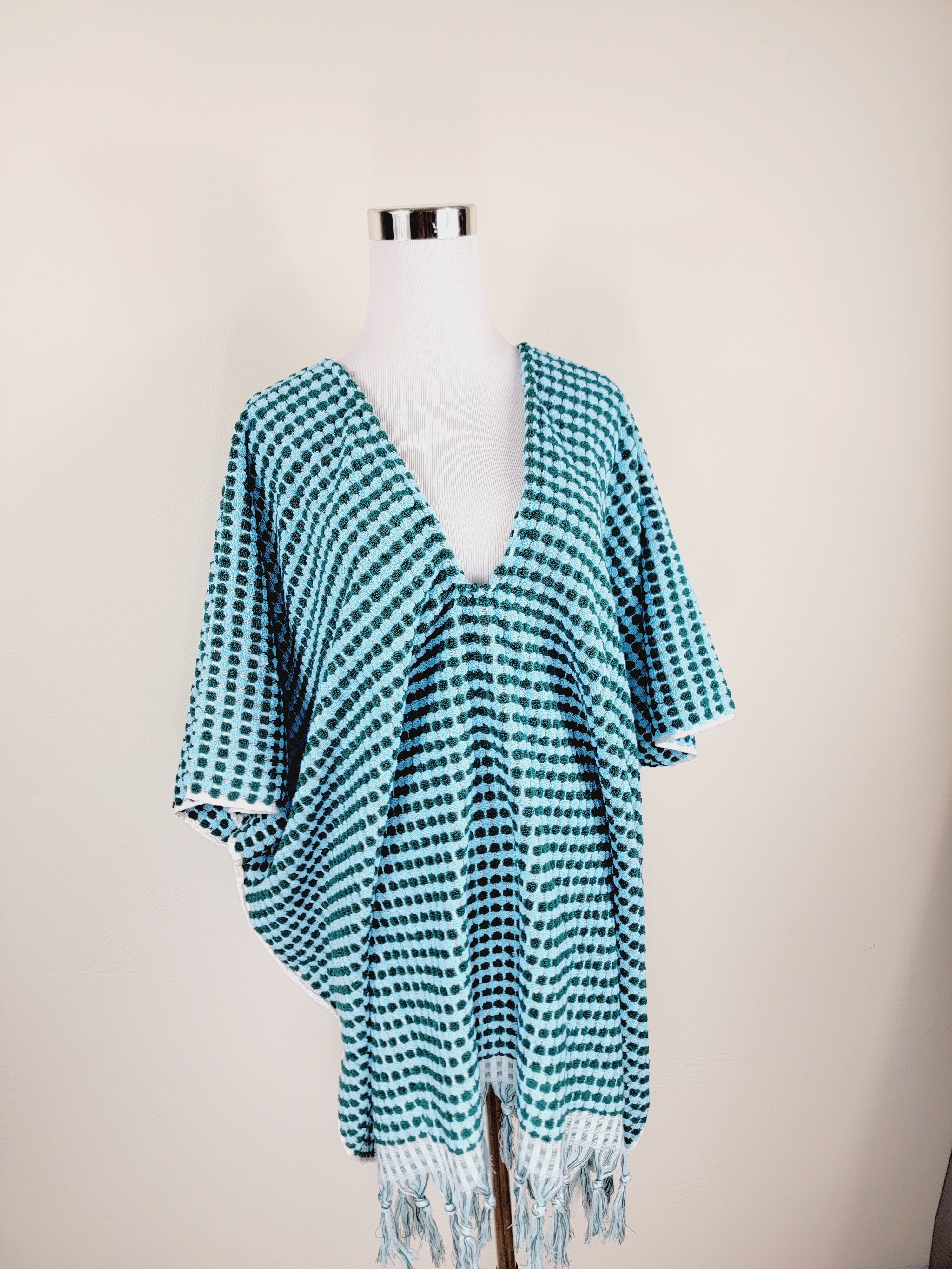 Green and white patterned poncho on a mannequin against a beige background