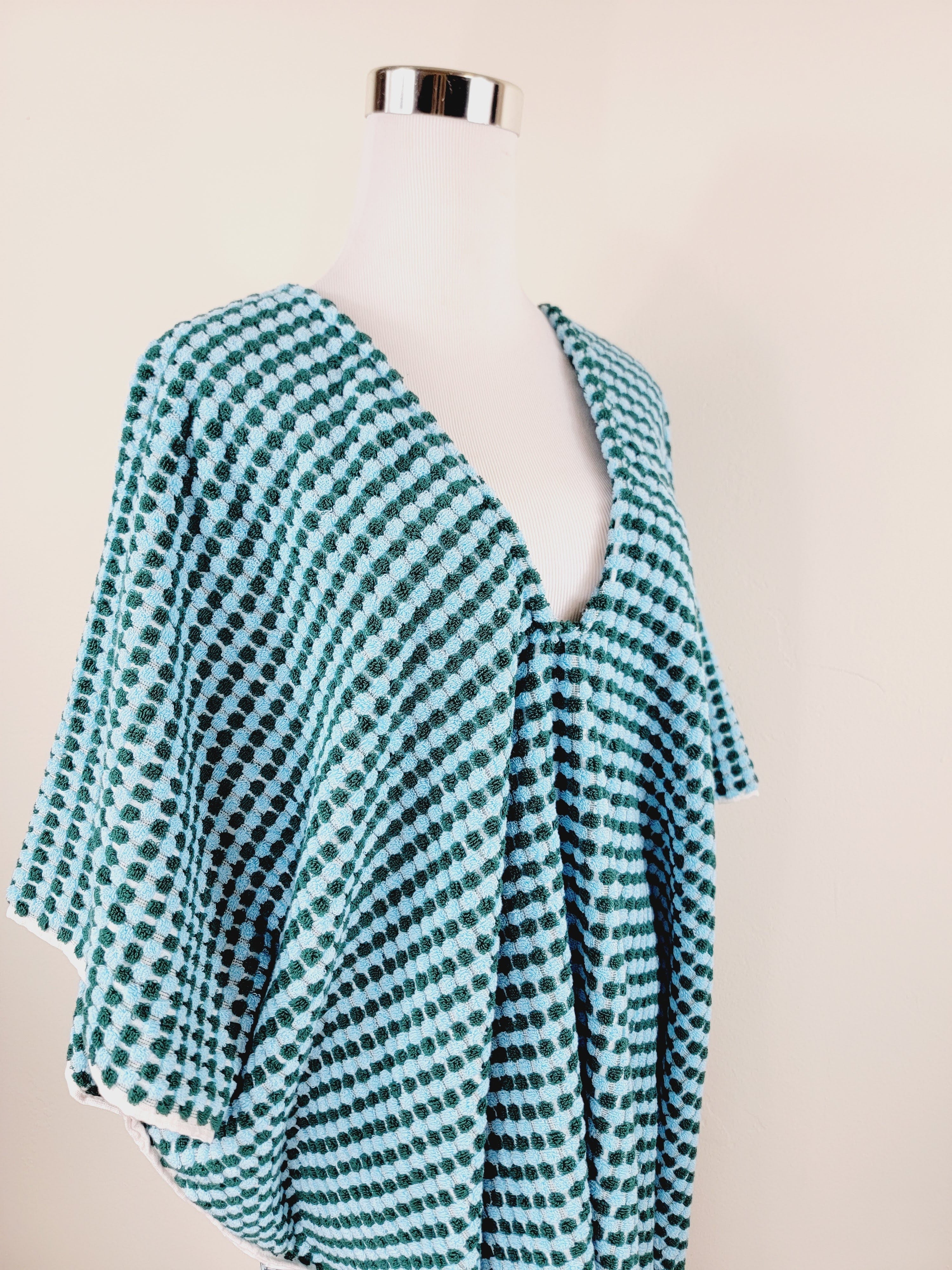 Teal and white patterned poncho on a mannequin against a beige background