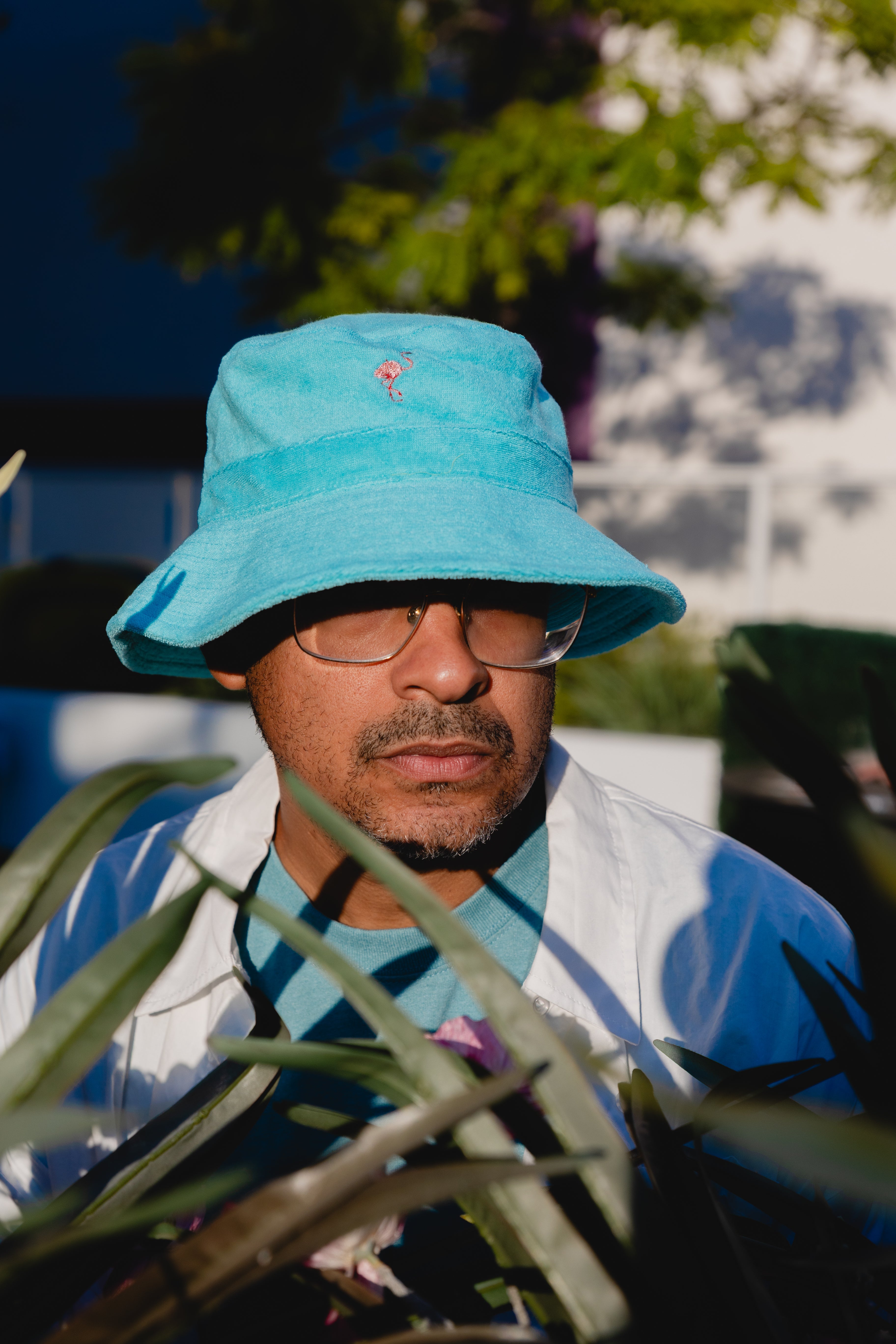 Person wearing a blue bucket hat and glasses, standing among plants with a blurred background