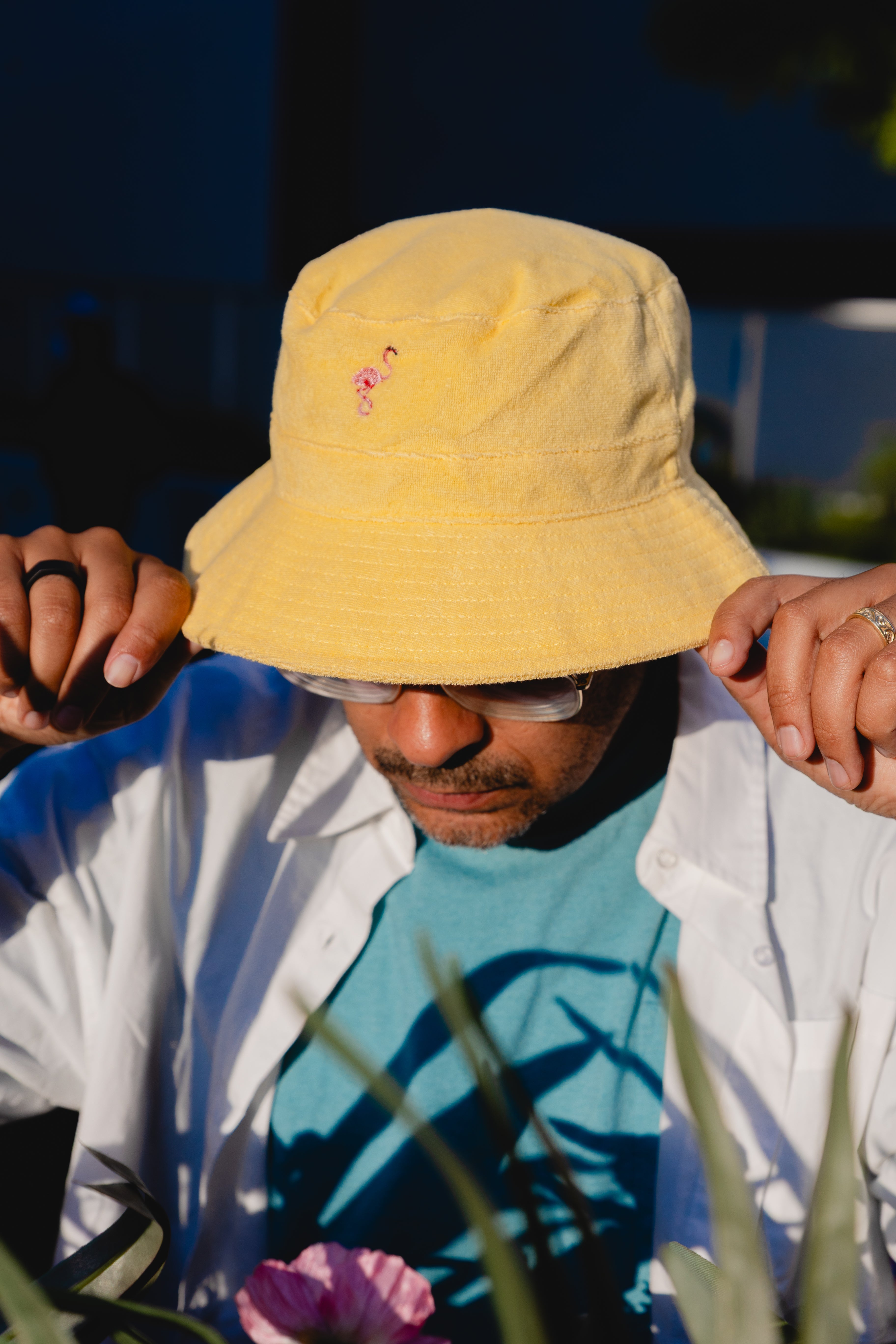 Person wearing a yellow bucket hat with a pink flower design, standing outdoors.