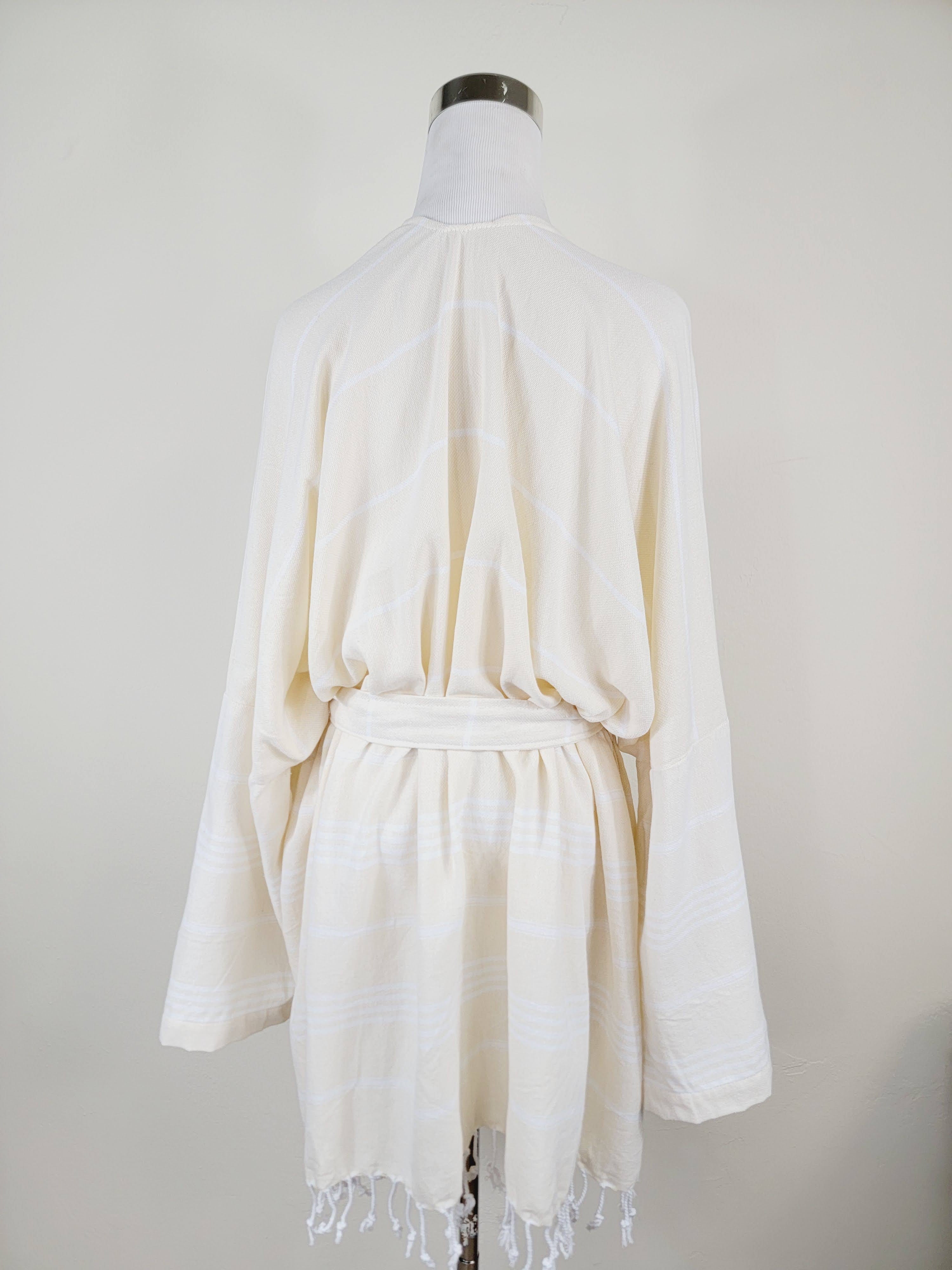White robe with fringe on a mannequin against a plain background