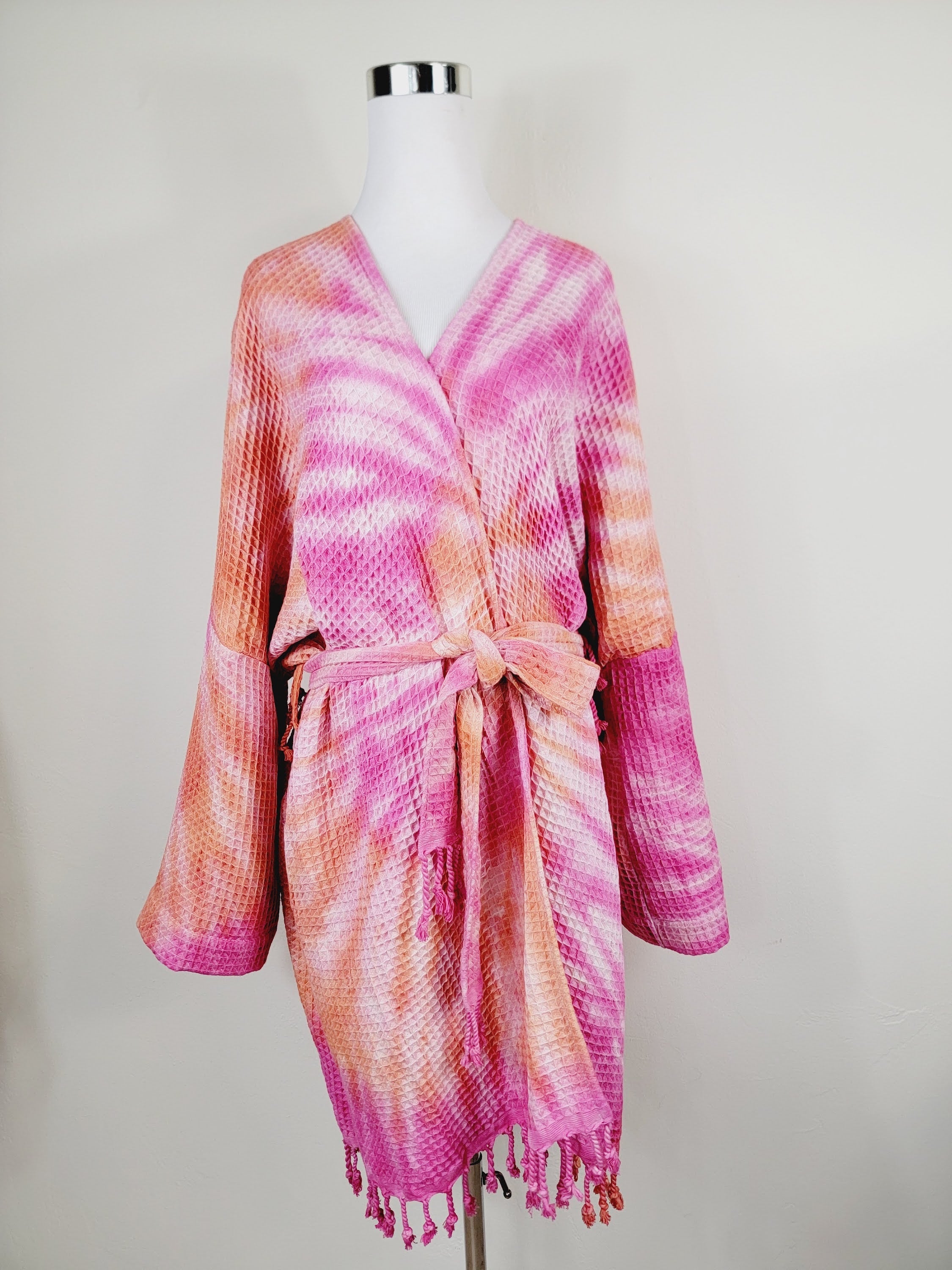 Tie-dye robe with pink and orange pattern on a mannequin against a white background