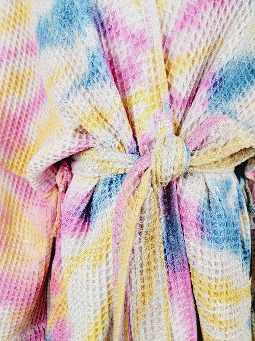 Close-up of a colorful textured fabric with a knot, featuring pink, blue, and yellow hues.
