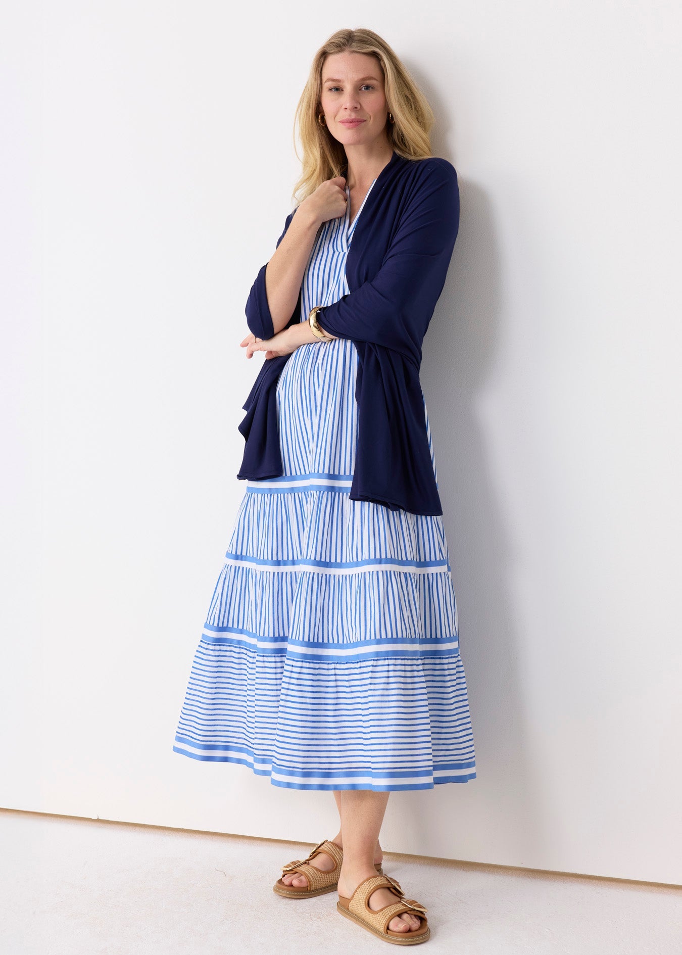 Woman wearing a blue and white striped dress with a navy cardigan against a white background
