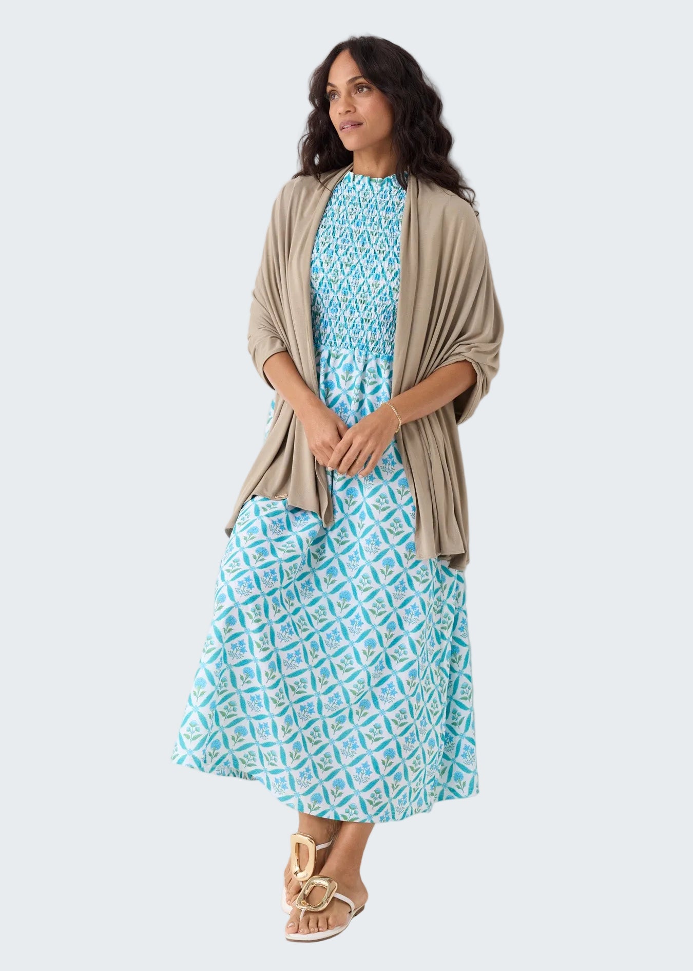 Woman wearing a blue patterned dress with a beige cardigan against a white background
