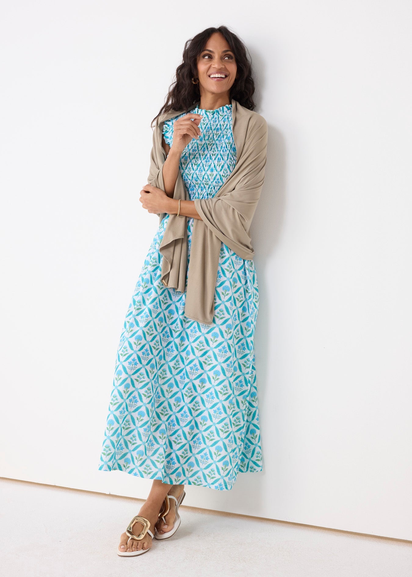 Woman wearing a blue patterned dress with a beige cardigan against a white background