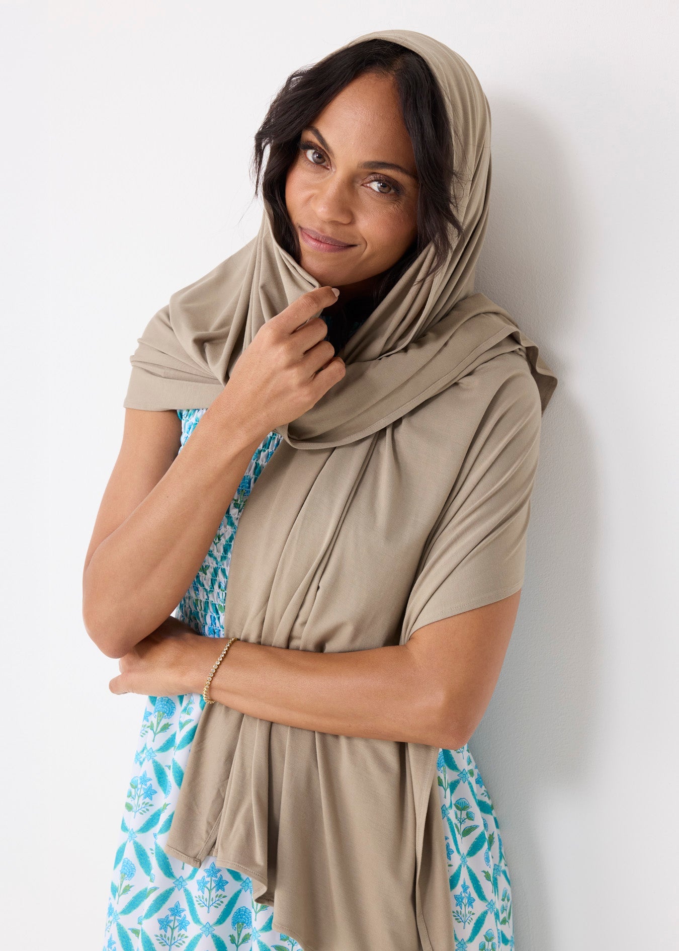 Woman wearing a beige hijab and a colorful dress against a white background
