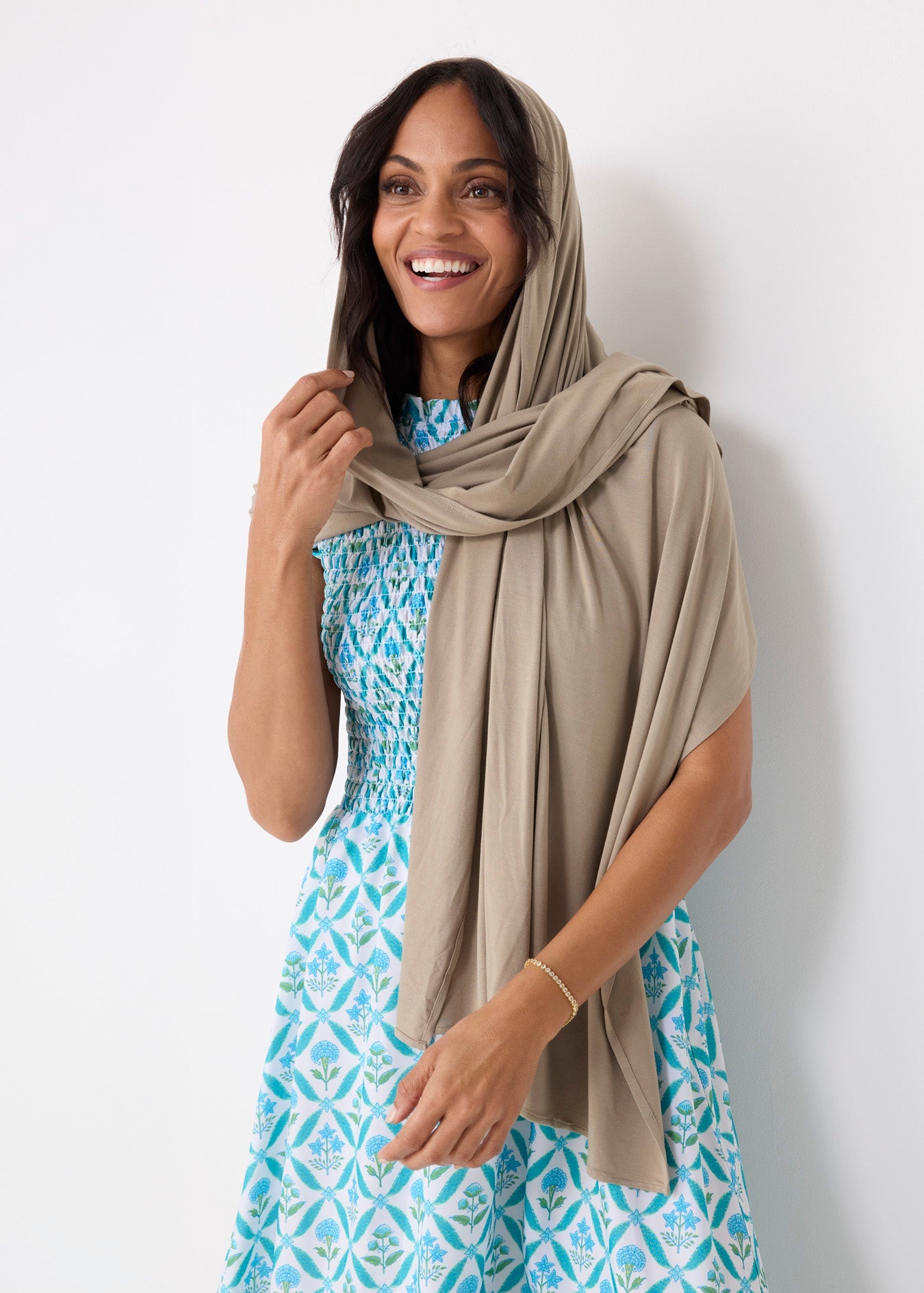 Woman wearing a blue patterned dress with a beige hijab against a white background