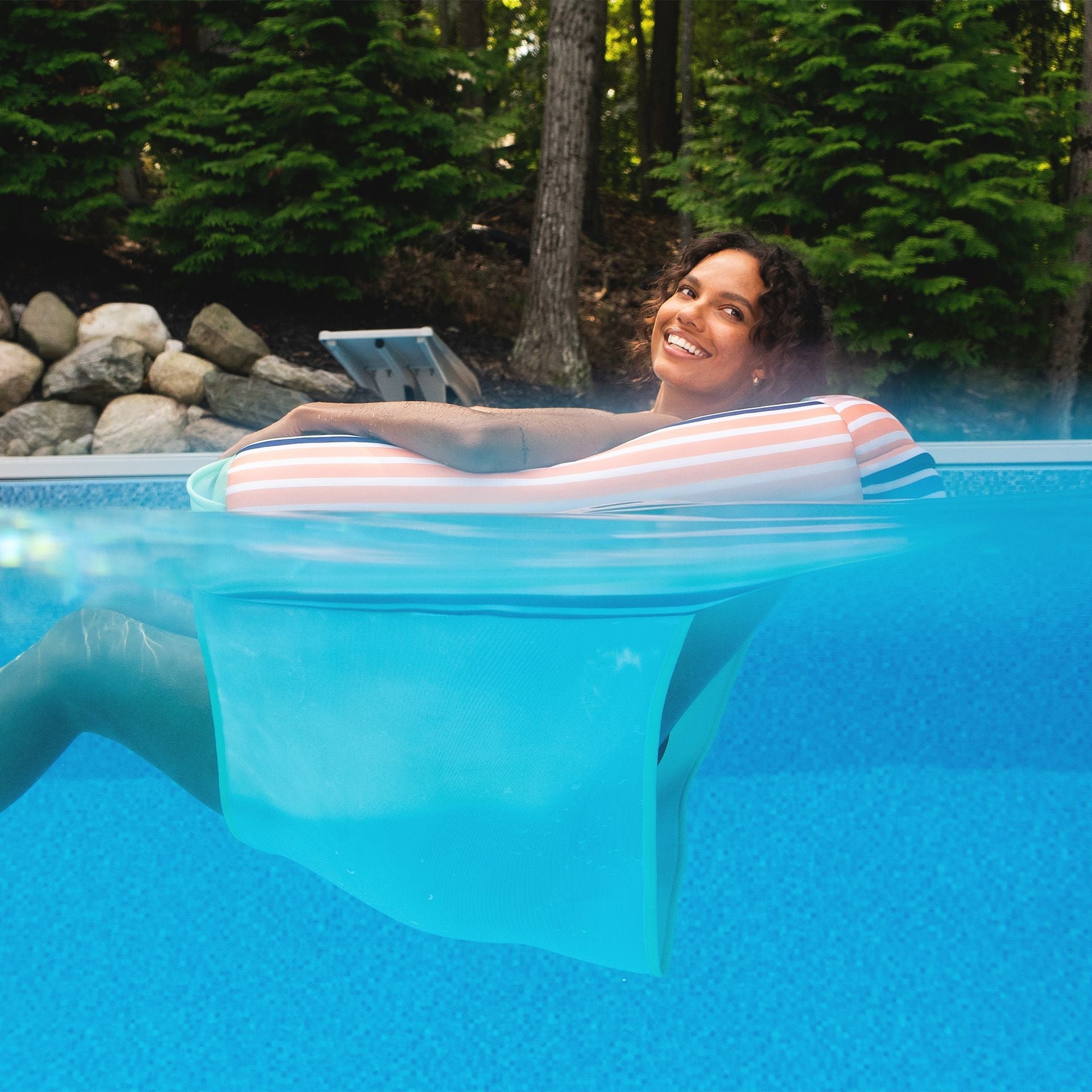 Woman relaxing in a pool with an inflatable lounge, surrounded by trees and rocks.
