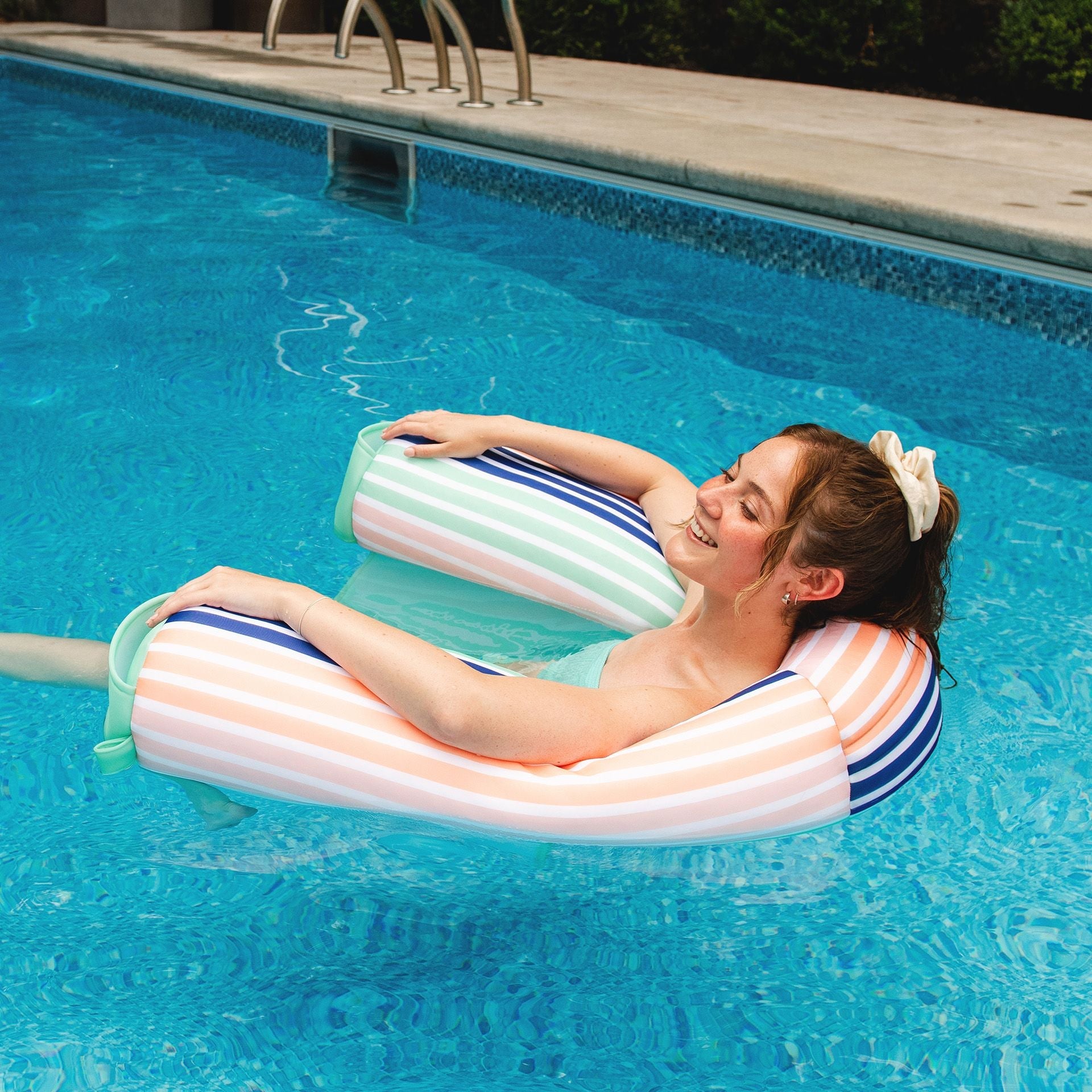 Woman relaxing on a striped inflatable pool float in a swimming pool.