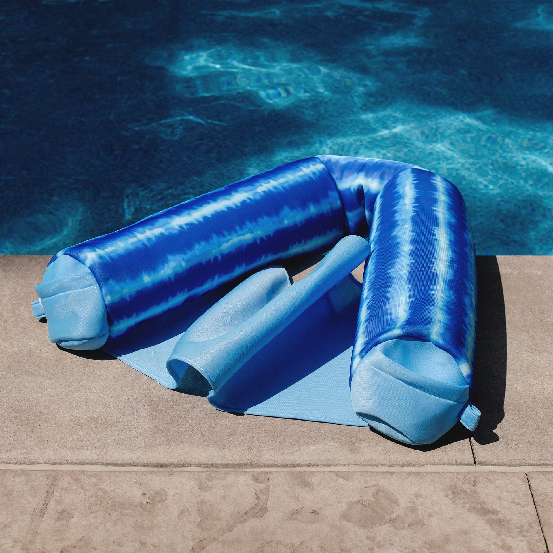 Blue inflatable pool float shaped like a person lying on a poolside.