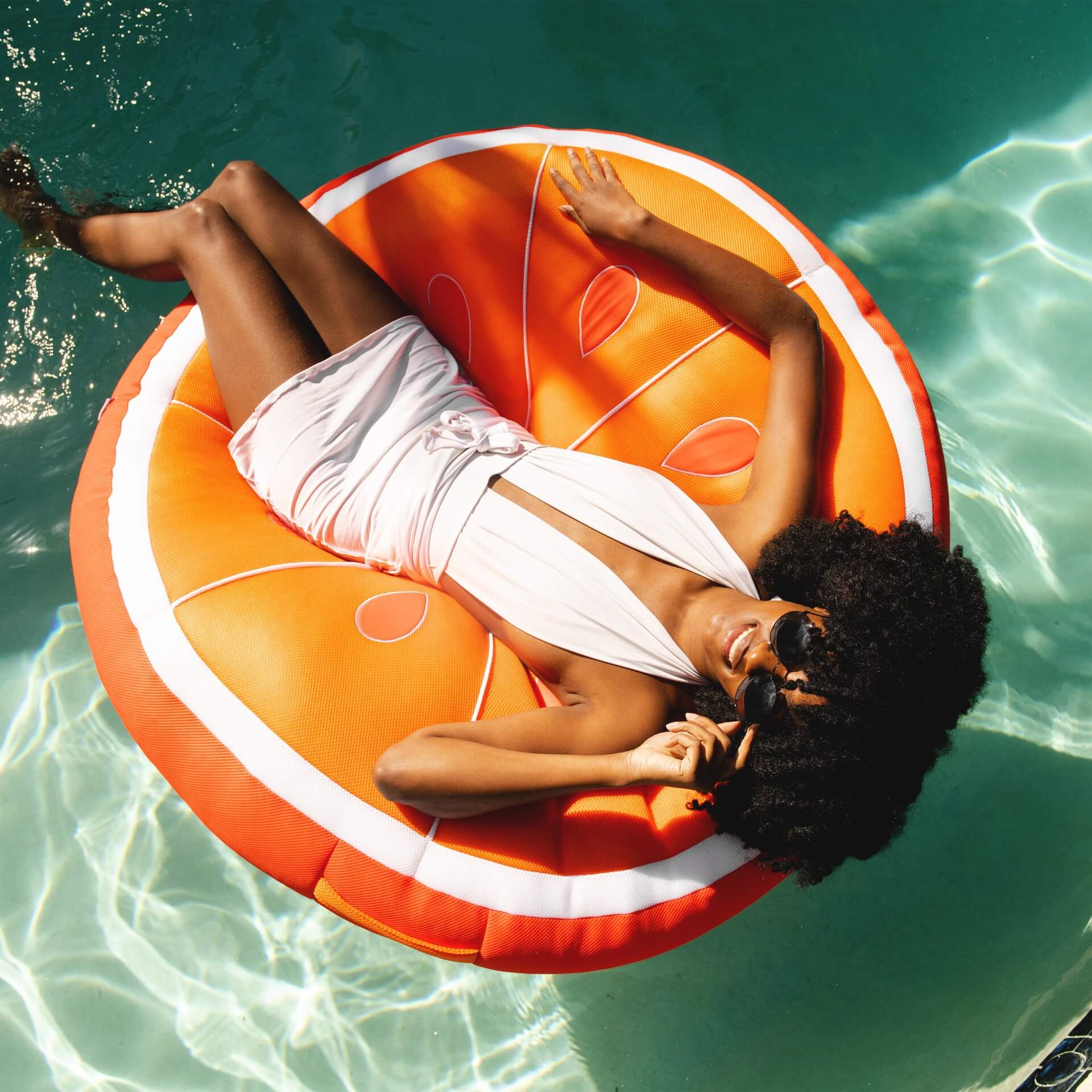Woman lounging on a pineapple-shaped inflatable pool float in clear blue water.