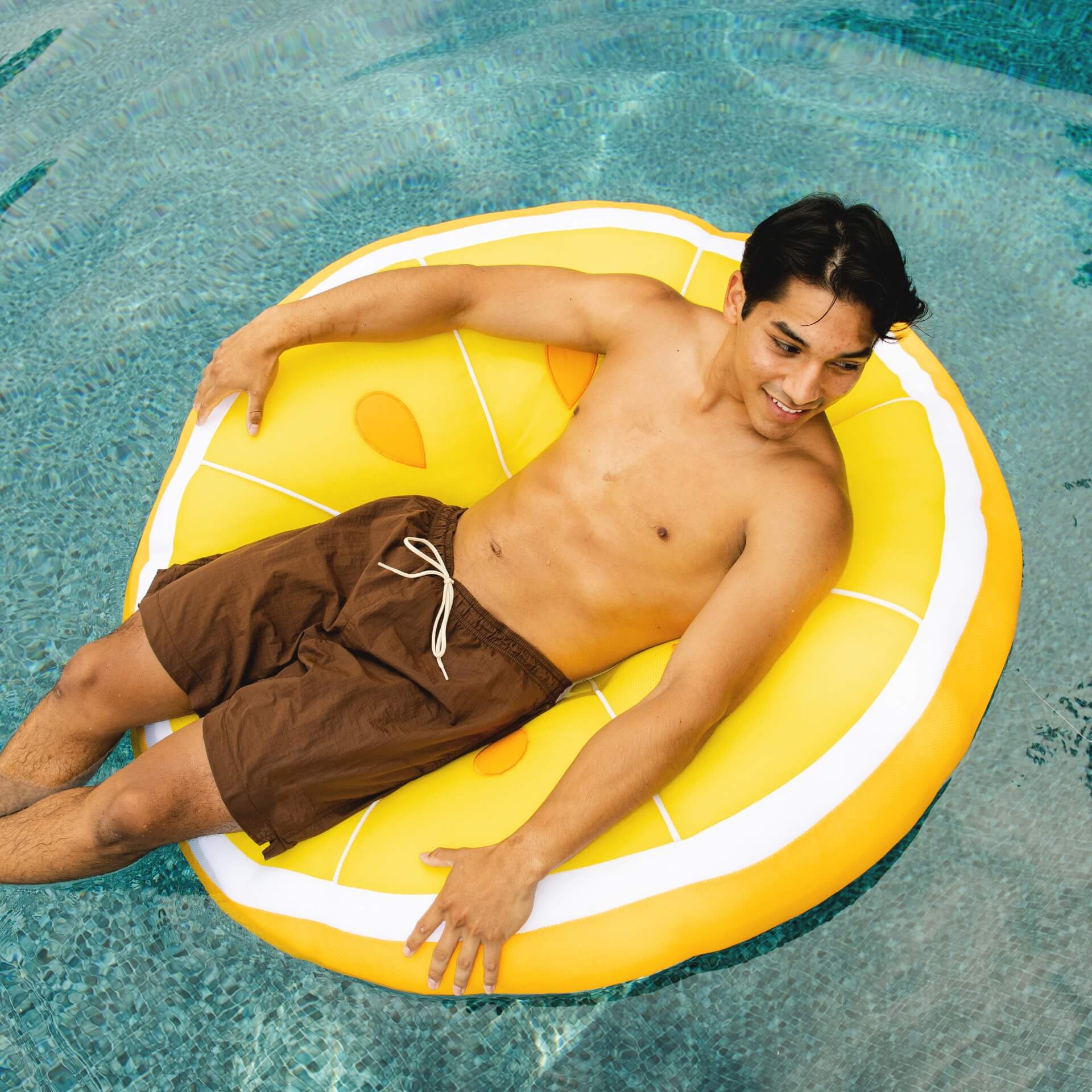 Man lying on a yellow pineapple-shaped pool float in clear blue water
