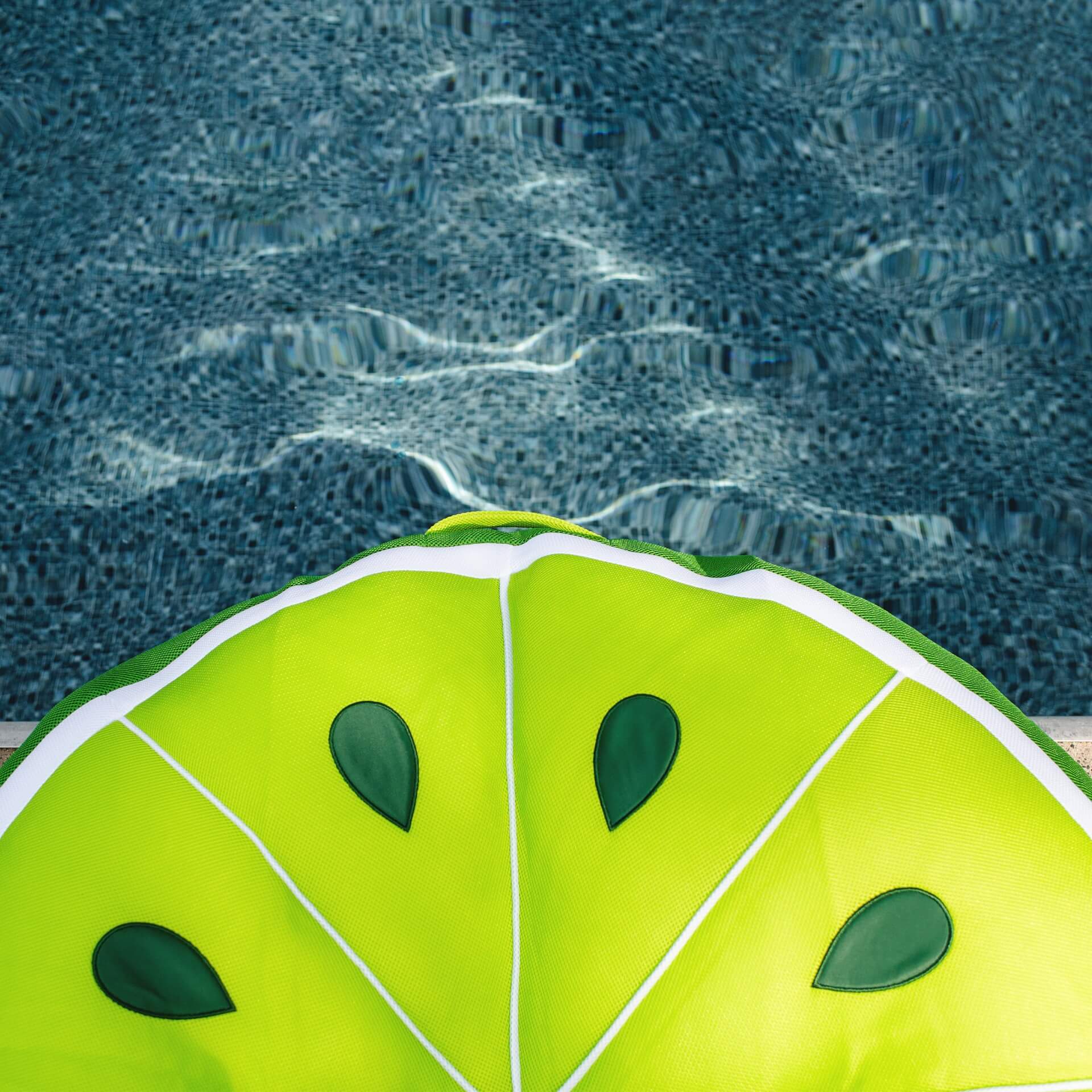 Green inflatable pool toy shaped like a lime wedge by a pool.