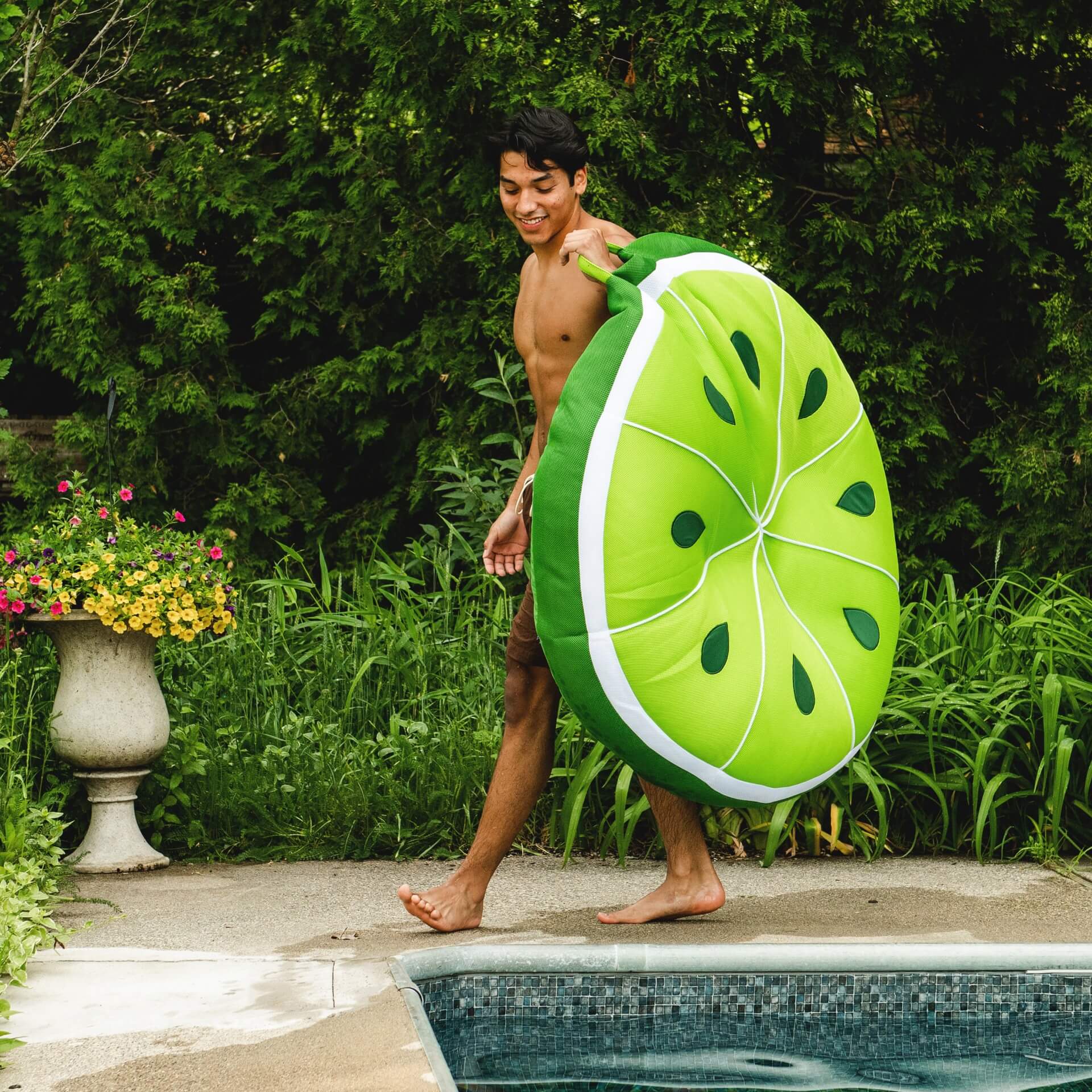 Man holding a lime-shaped pool float by a pool with greenery in the background