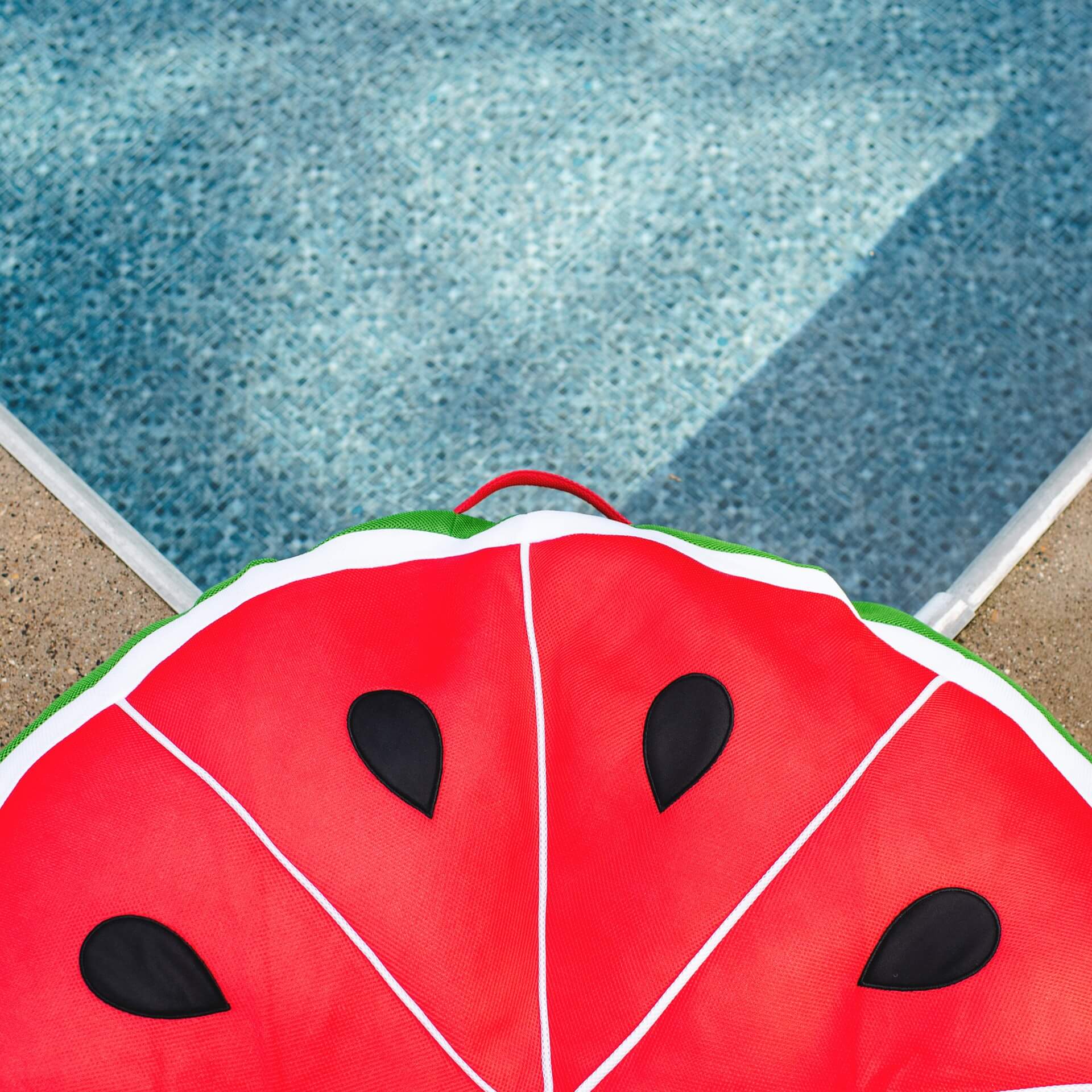 Red watermelon slice pool float on a pool deck.