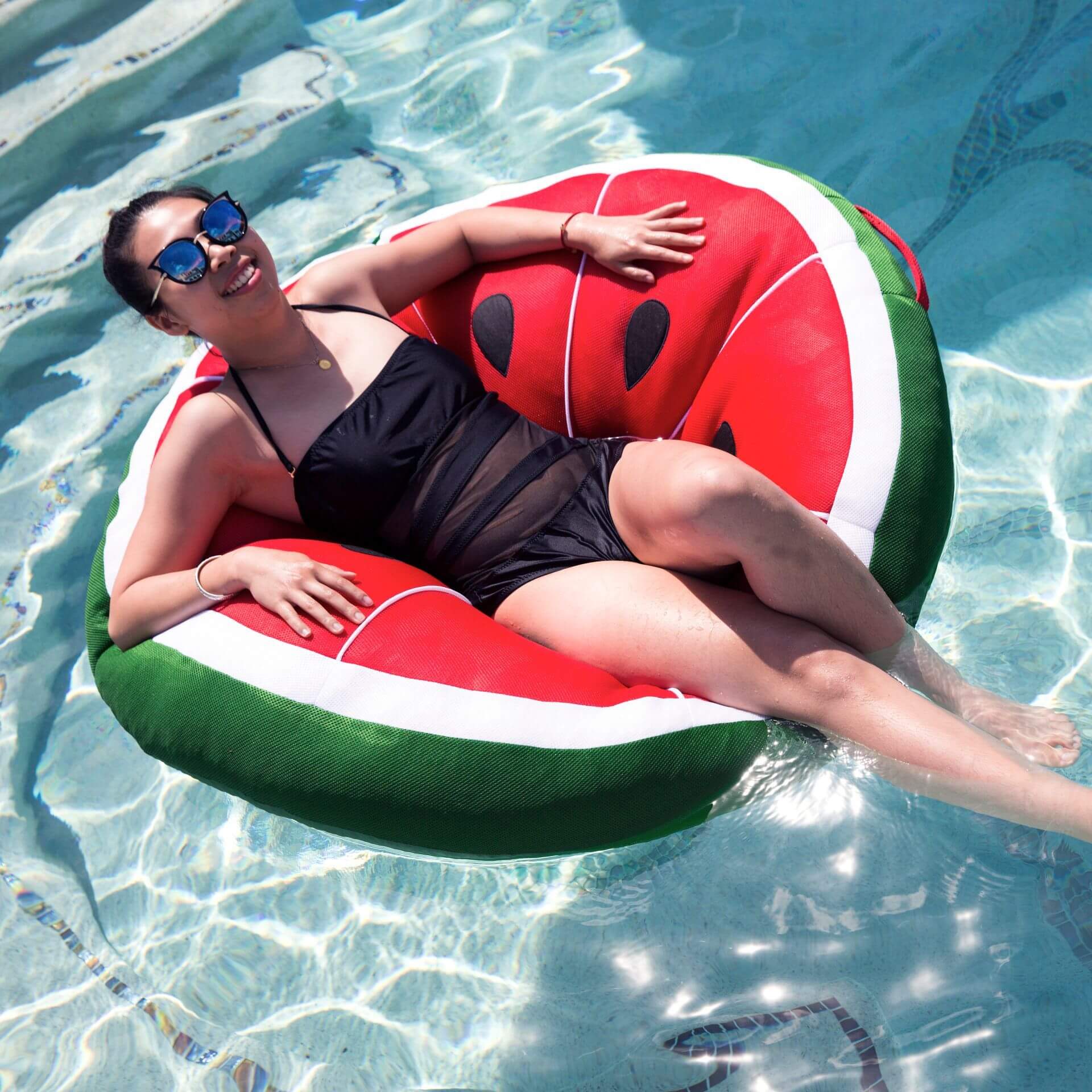 Woman lounging on a watermelon-shaped inflatable pool float in clear blue water.
