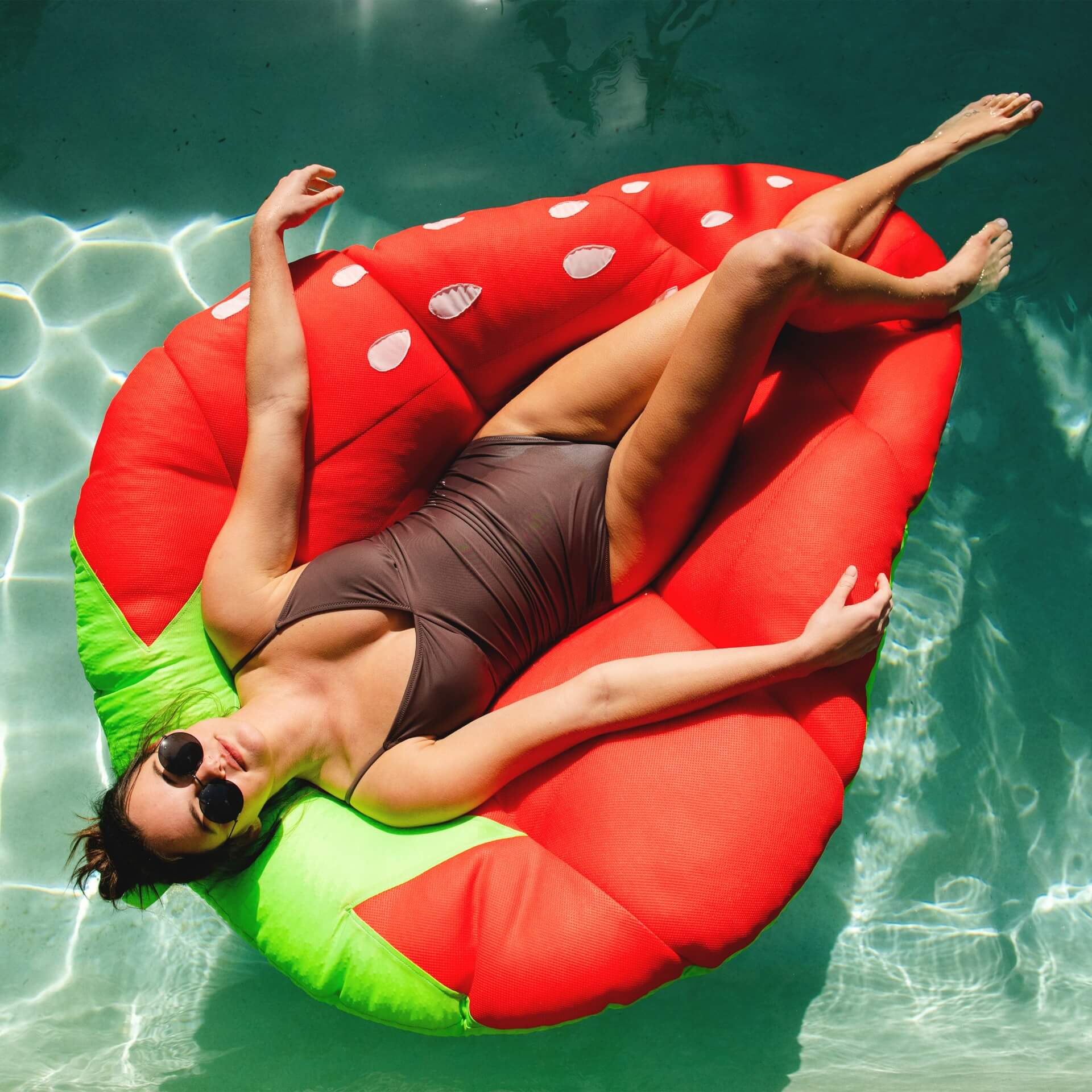 Woman lying on a watermelon-shaped inflatable pool float in clear blue water.