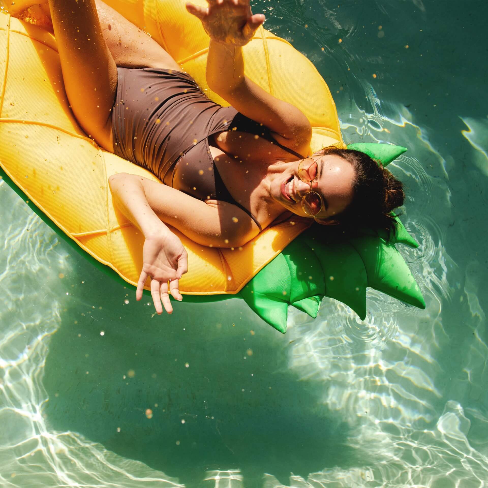 Woman lying on a pineapple-shaped inflatable raft in clear water