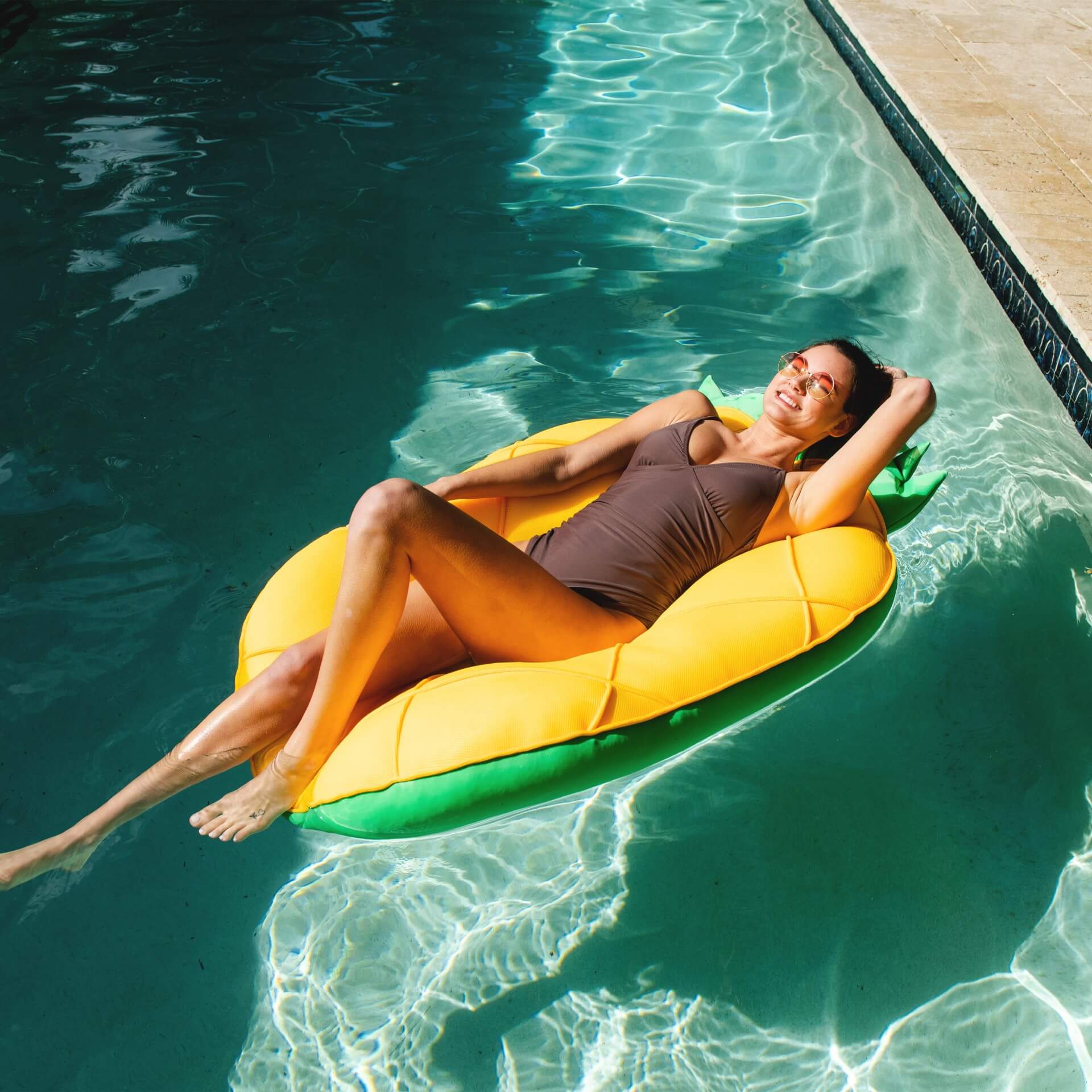 Woman lounging on a yellow and green inflatable pool float in a pool.