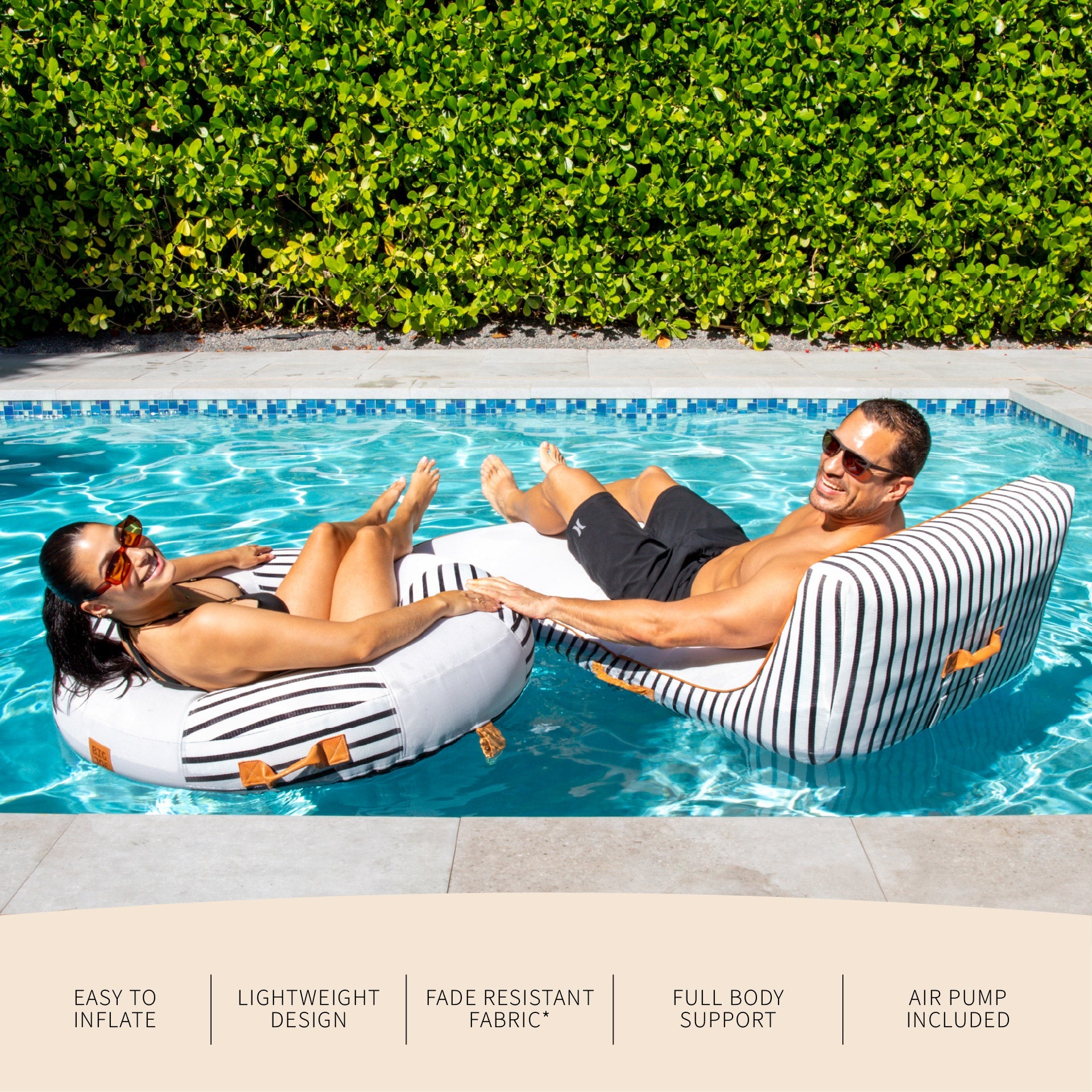 Two people lounging on striped pool floats in a swimming pool with greenery in the background.