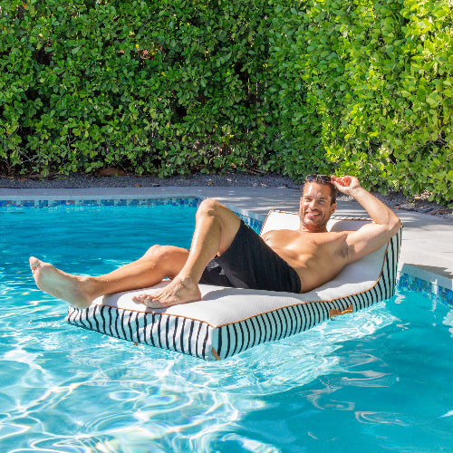 Man relaxing on a striped pool float in a swimming pool with greenery in the background