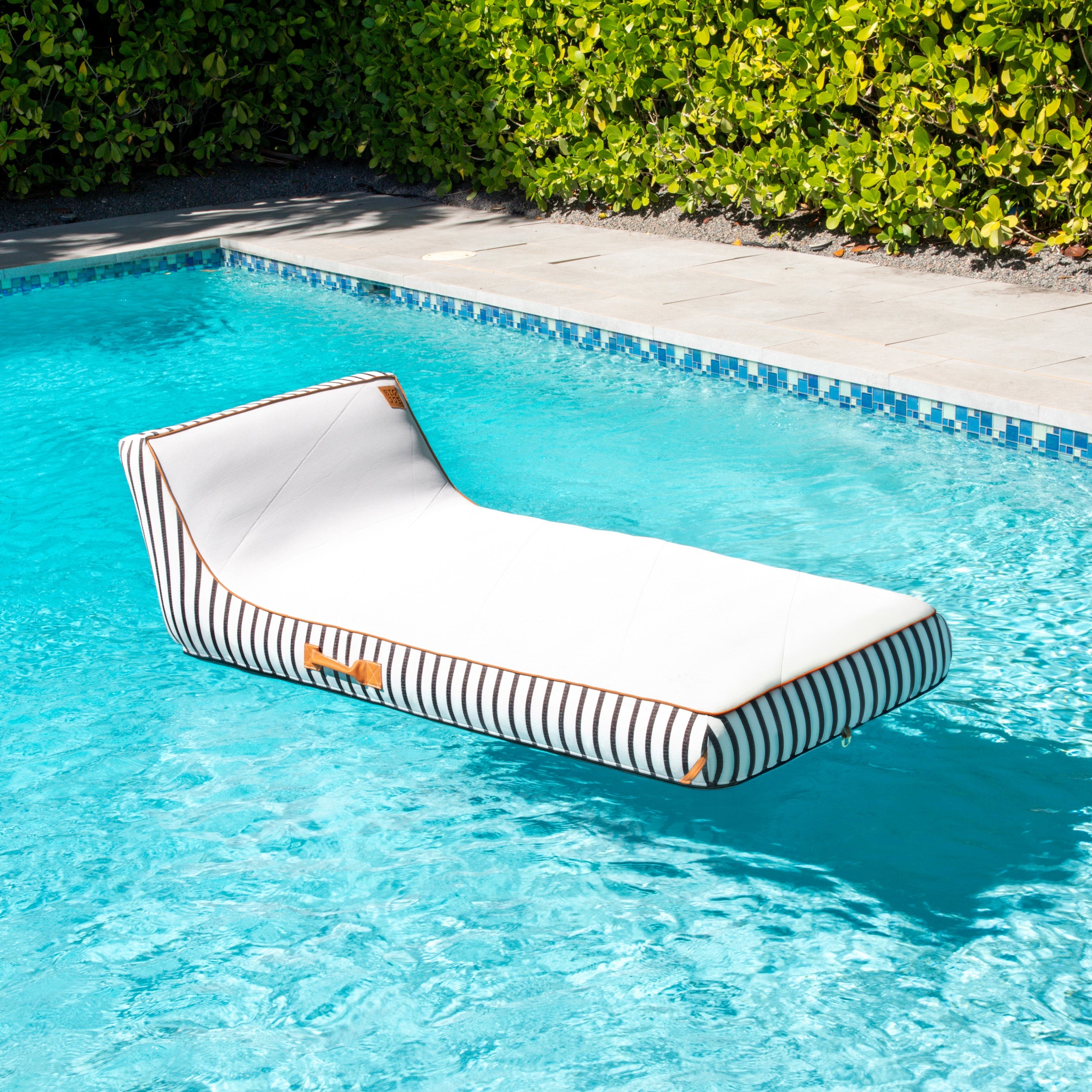 Striped pool float floating in a pool with greenery in the background