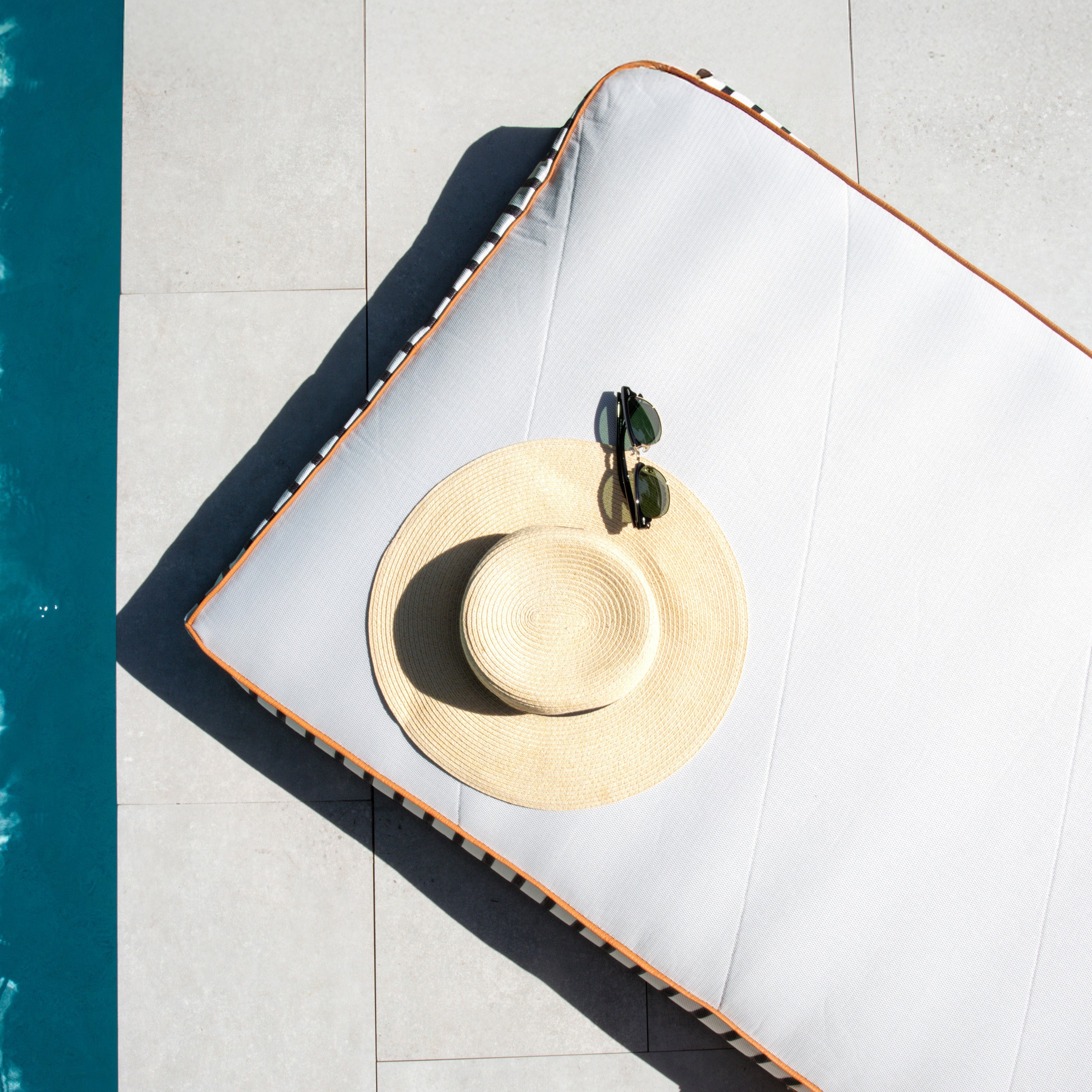 Straw hat with a green ribbon on a white surface next to a pool.