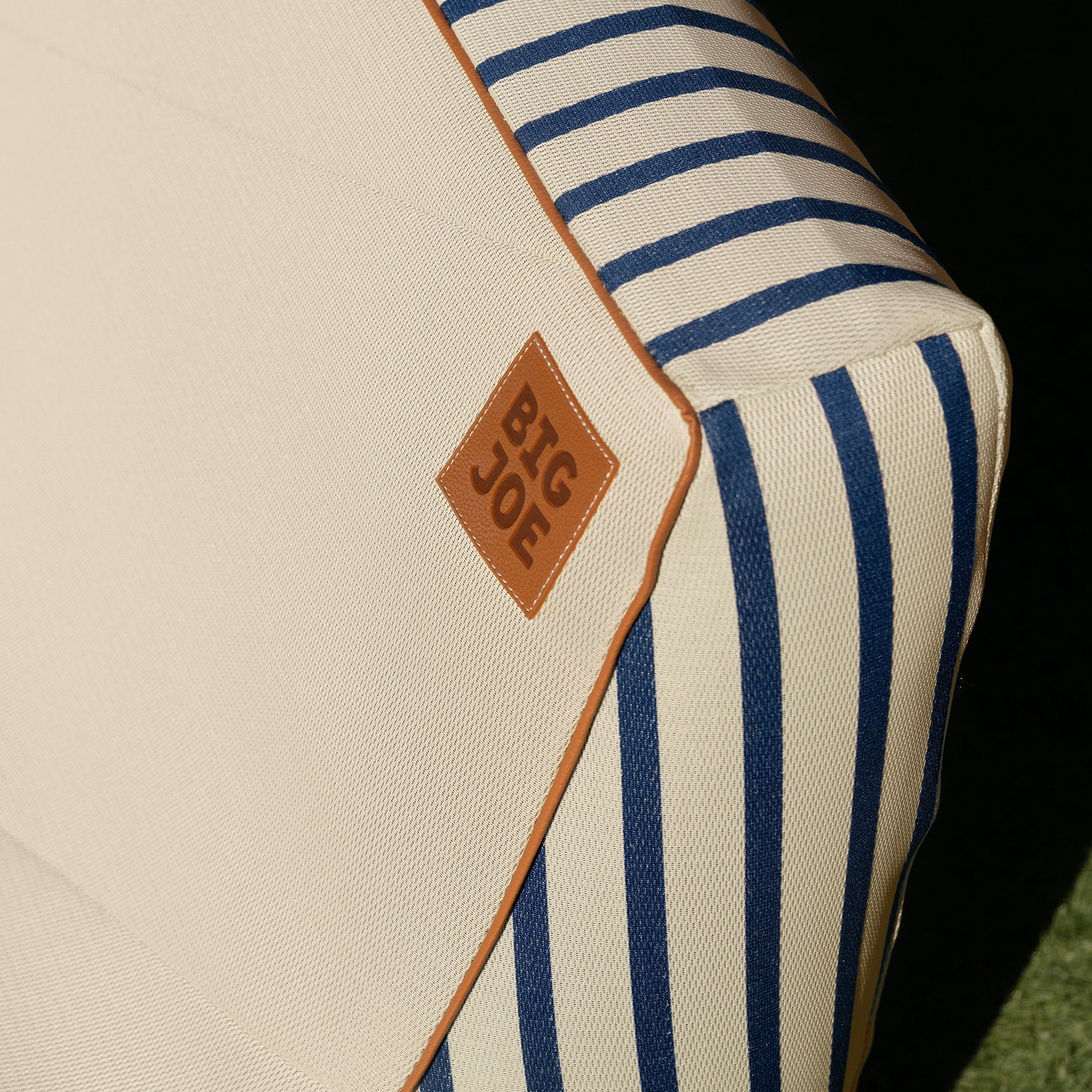 Beige and blue striped pet bed with a brown leather tag displaying 'BIG JOE' on a grass background.