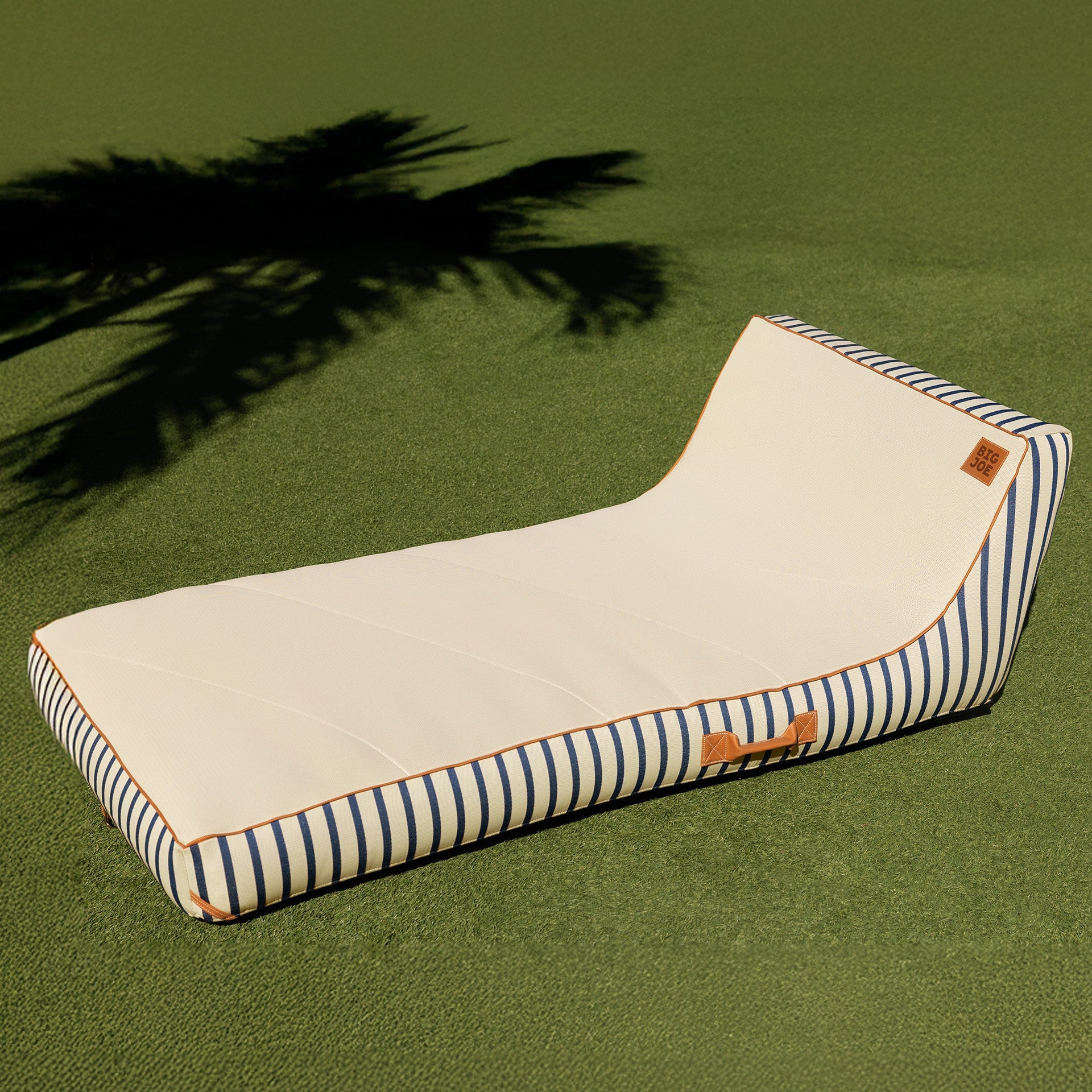 Striped pet bed on a green surface with palm tree shadow