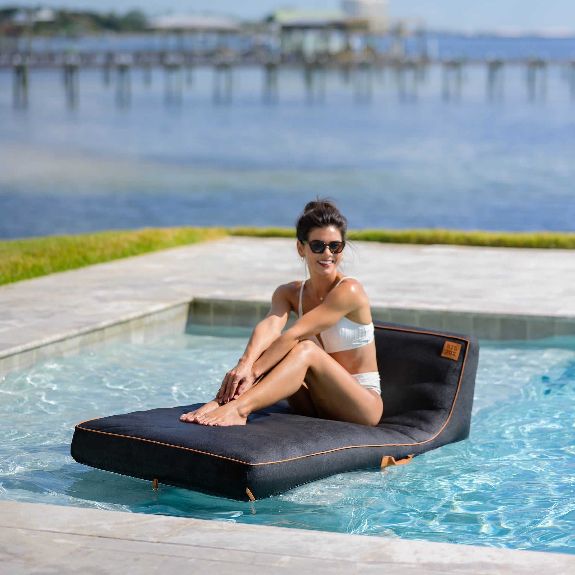 Woman sitting on a floating lounge by a pool with a scenic background