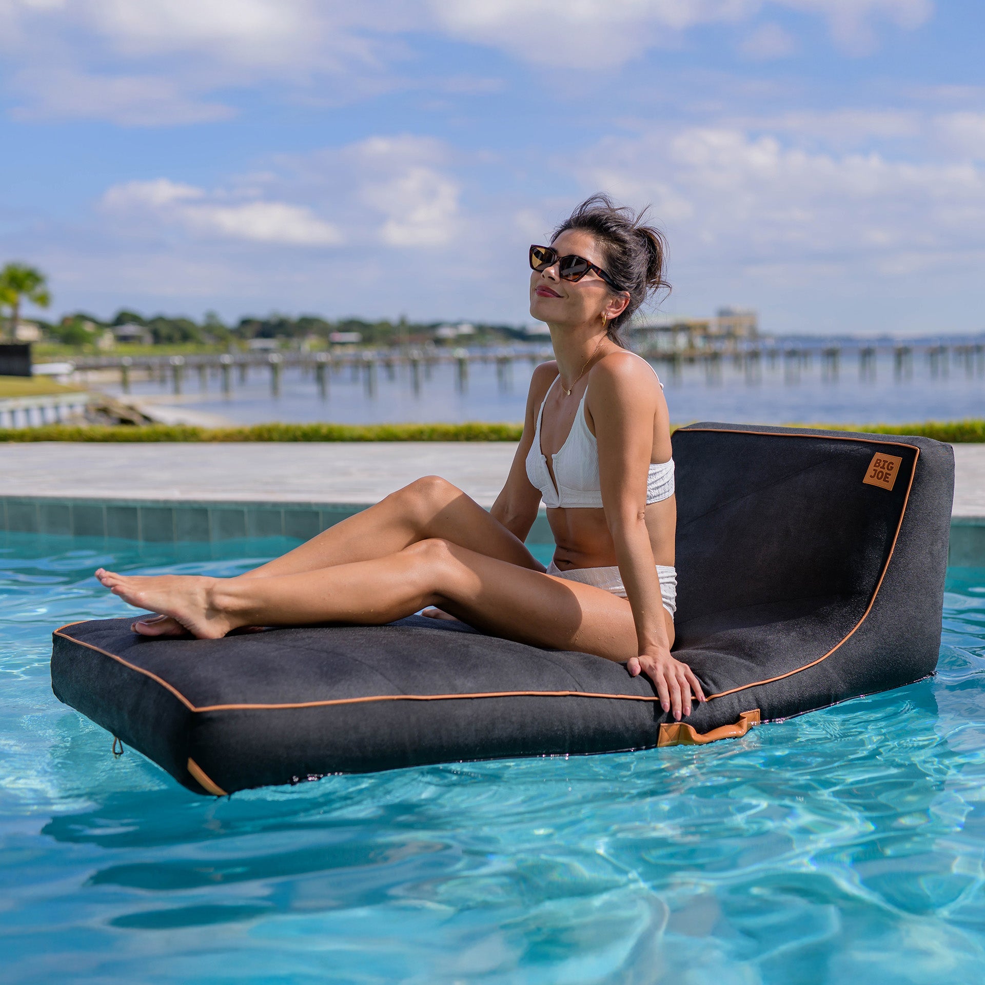 Woman relaxing on a floating inflatable lounger in a pool with a scenic background.