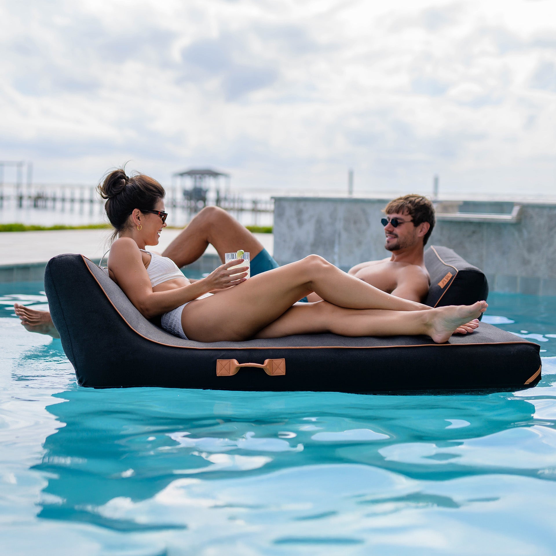 Two people relaxing on a inflatable pool float in a pool.