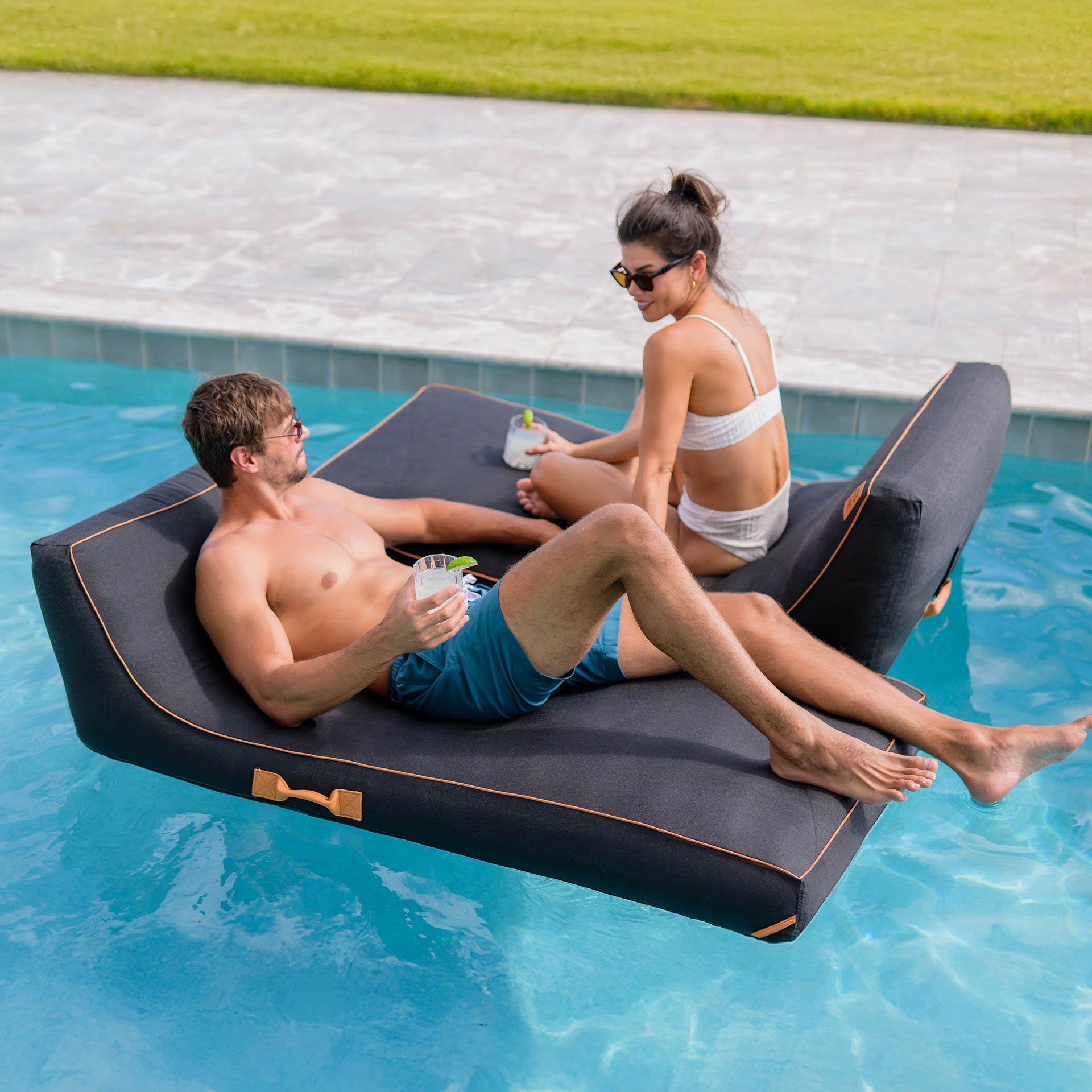Two people relaxing on a floating inflatable lounge in a pool.