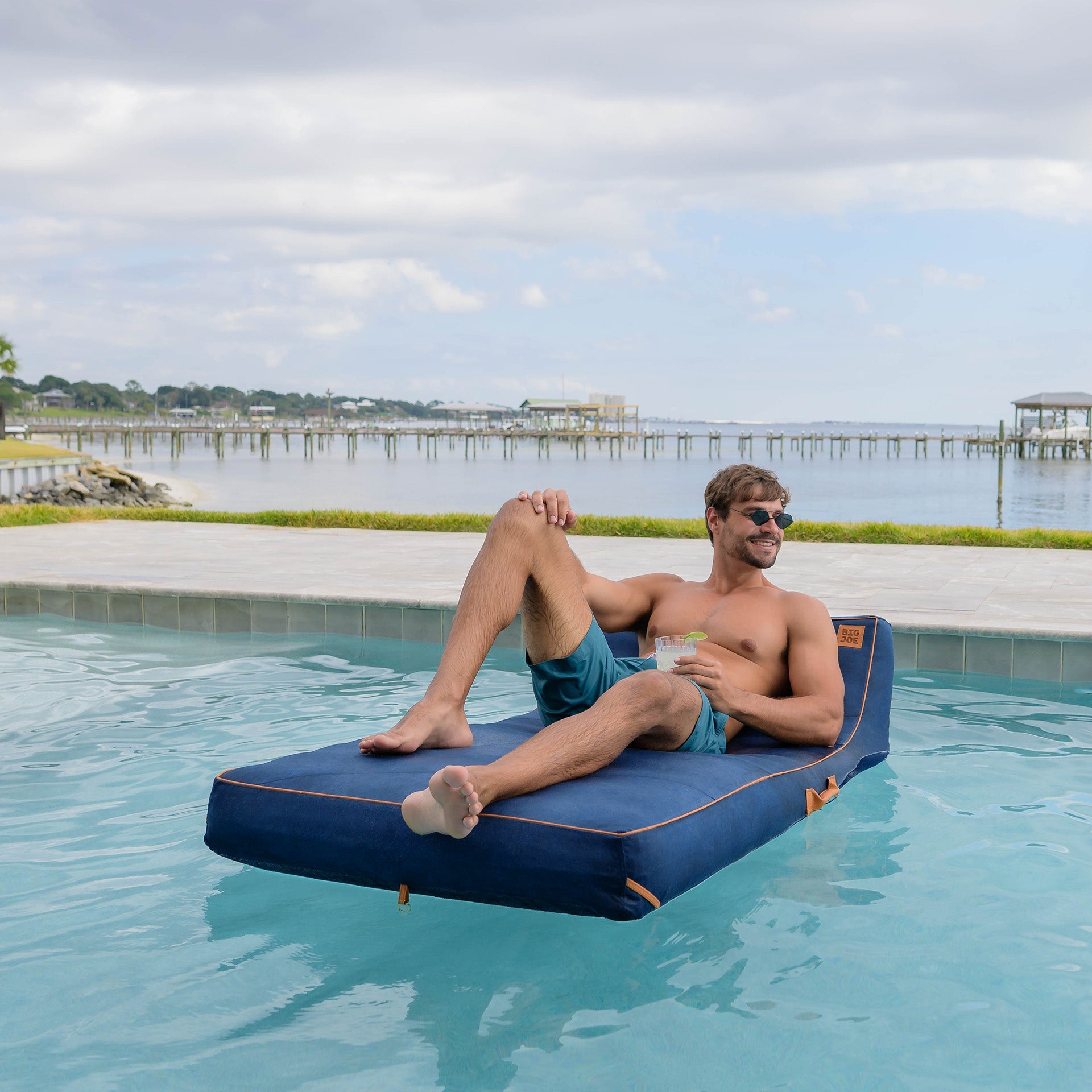 Man lounging on a blue inflatable pool float by a pool with a scenic background