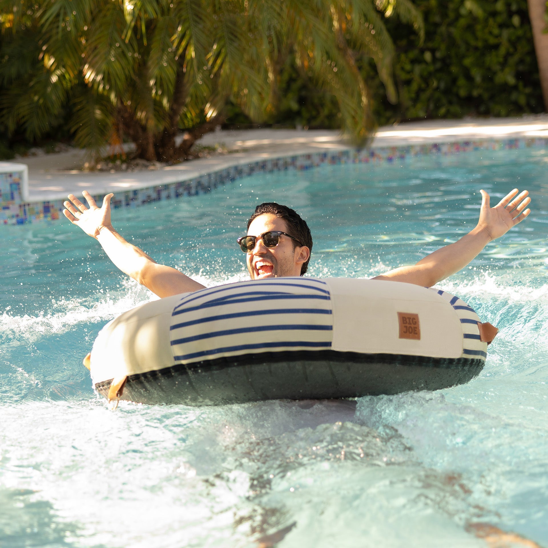 Person floating on a striped inner tube in a pool with greenery around