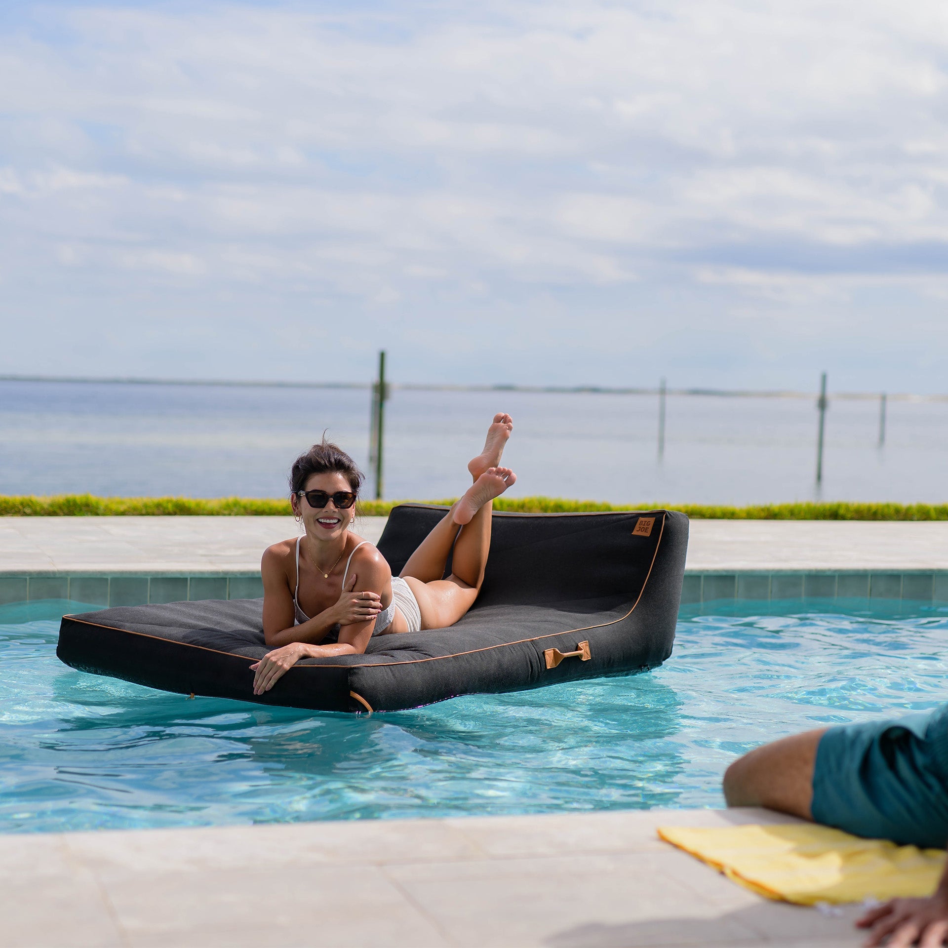 Woman lounging on a black inflatable pool float in a pool with a scenic background