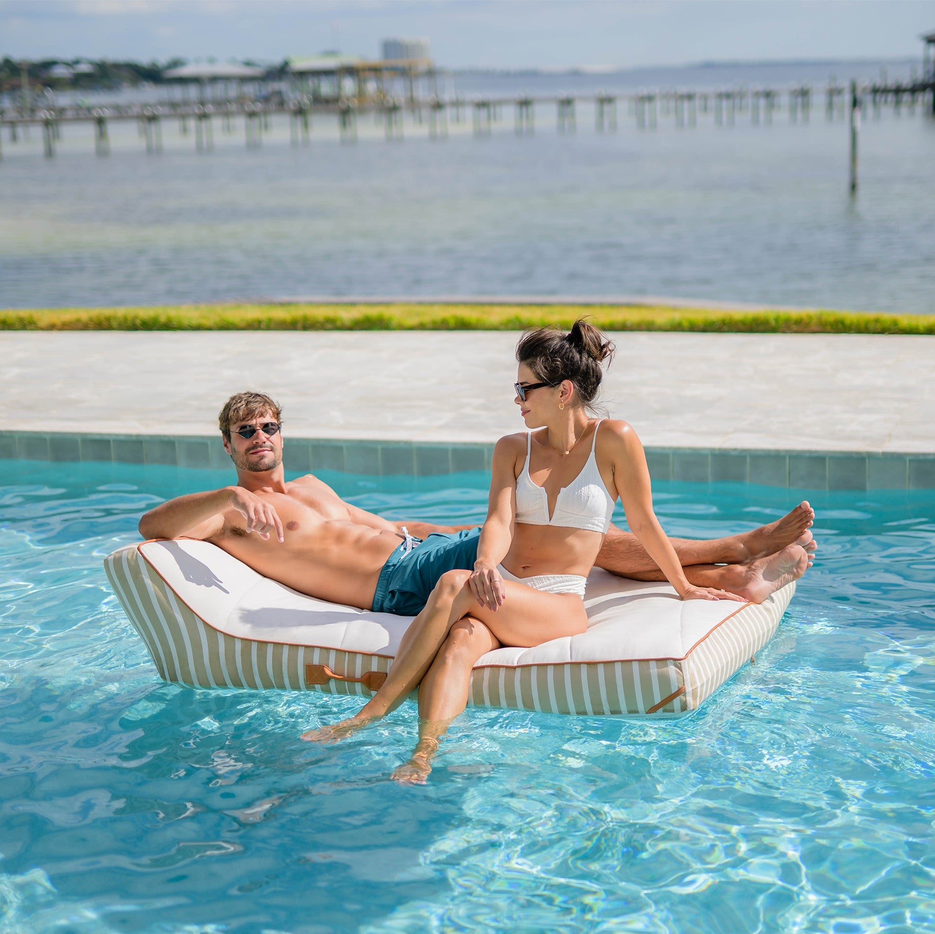 Two people relaxing on a pool float by a pool with a scenic background