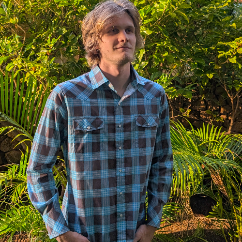 Man wearing a plaid shirt standing in front of green foliage