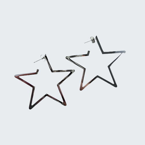A person's hand holding two silver-colored hoop earrings with a star shape on a wooden surface.